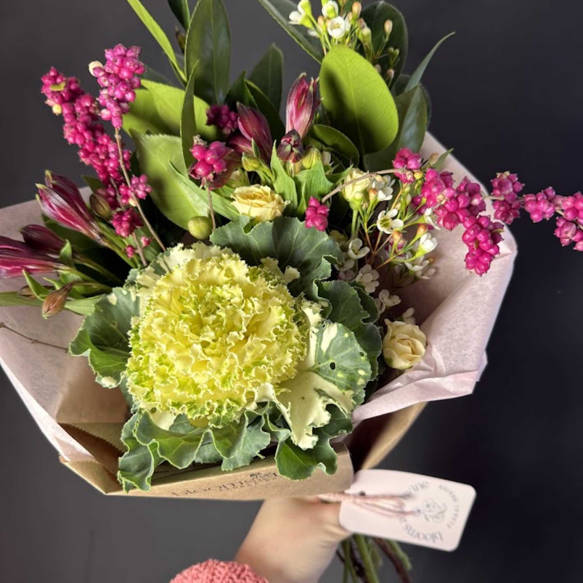Handheld bouquet with yellow-green carnations and pink flowers wrapped in paper