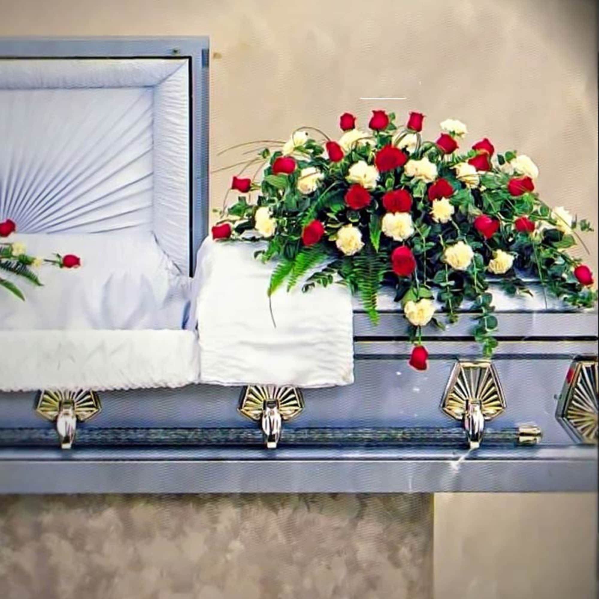 Red and white rose and carnation casket spray on a silver casket with greenery.