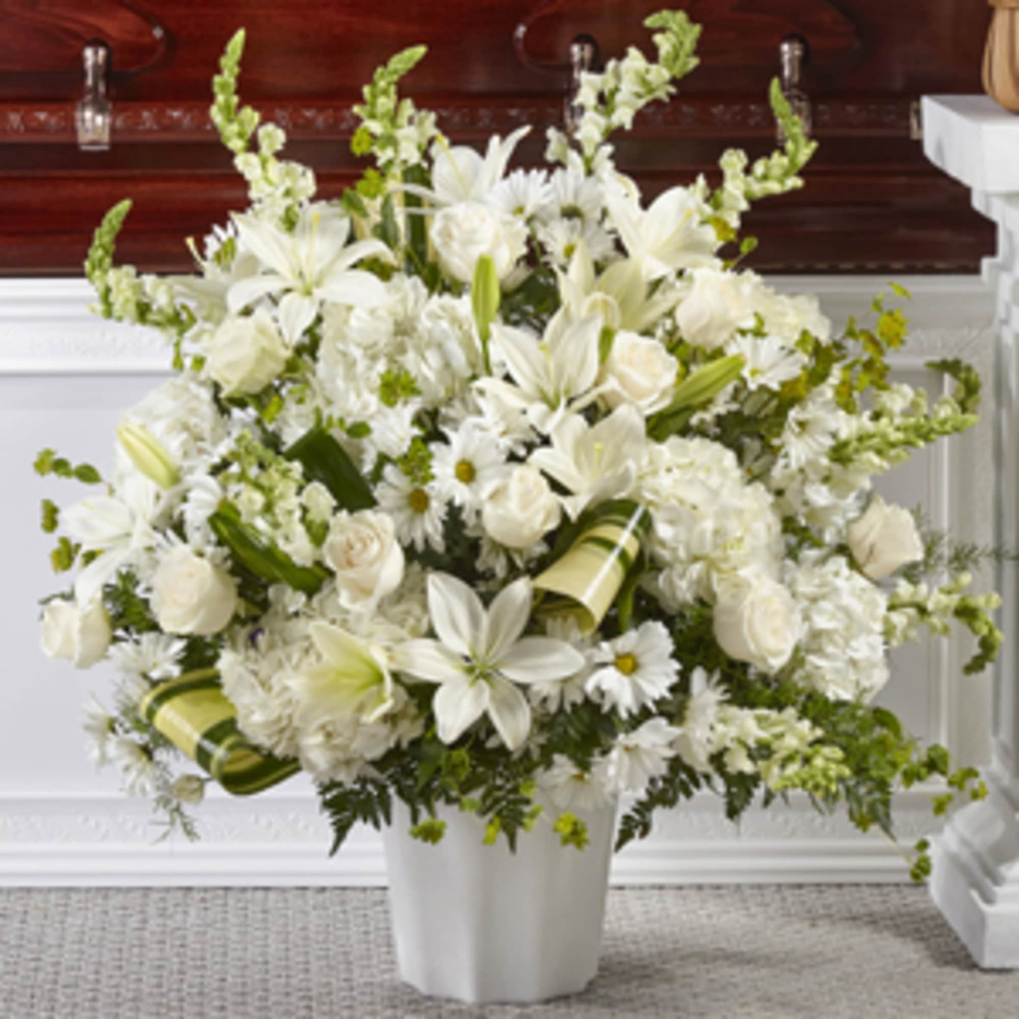 White floral arrangement in a white vase with lilies and roses