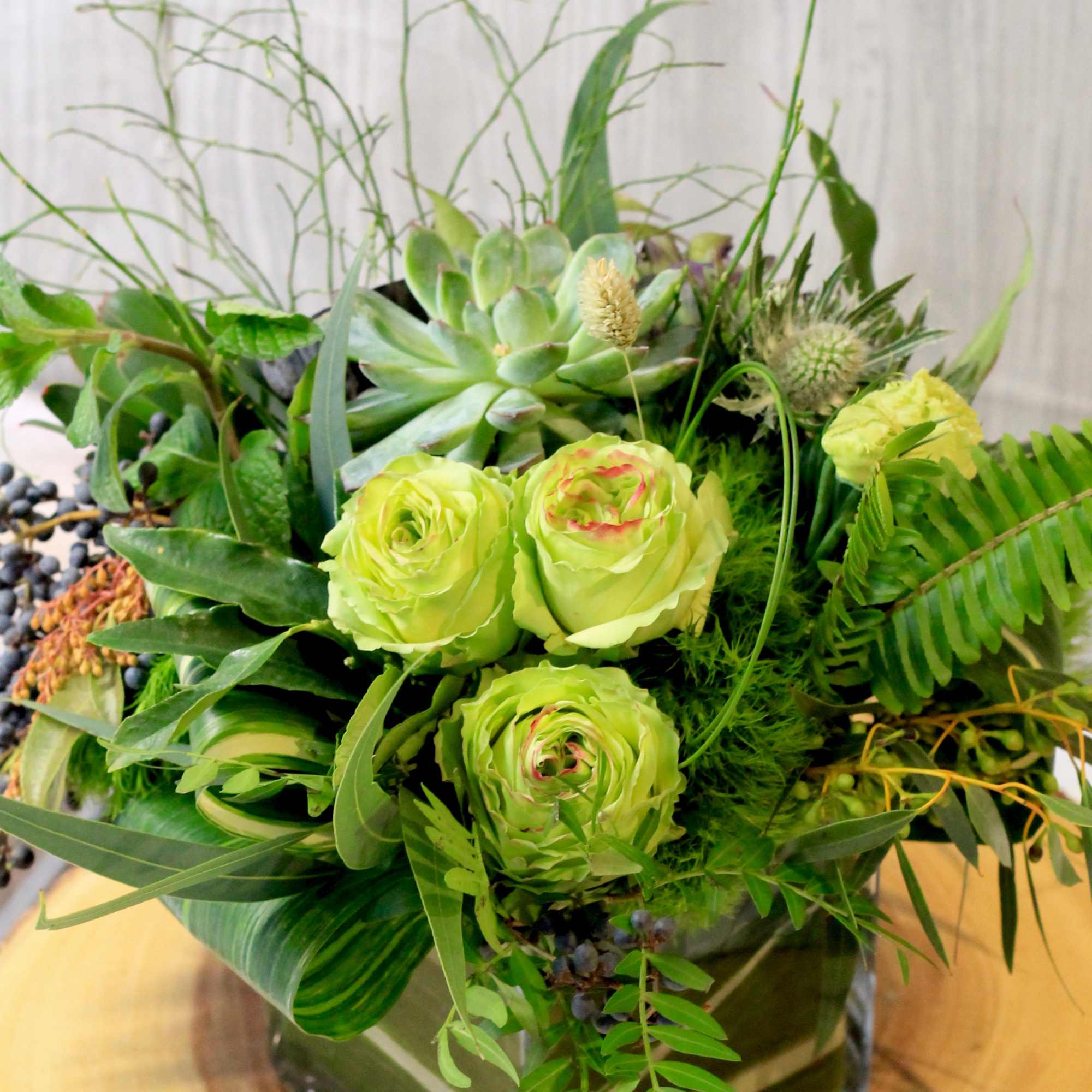 Green floral arrangement with roses and succulents in a glass vase