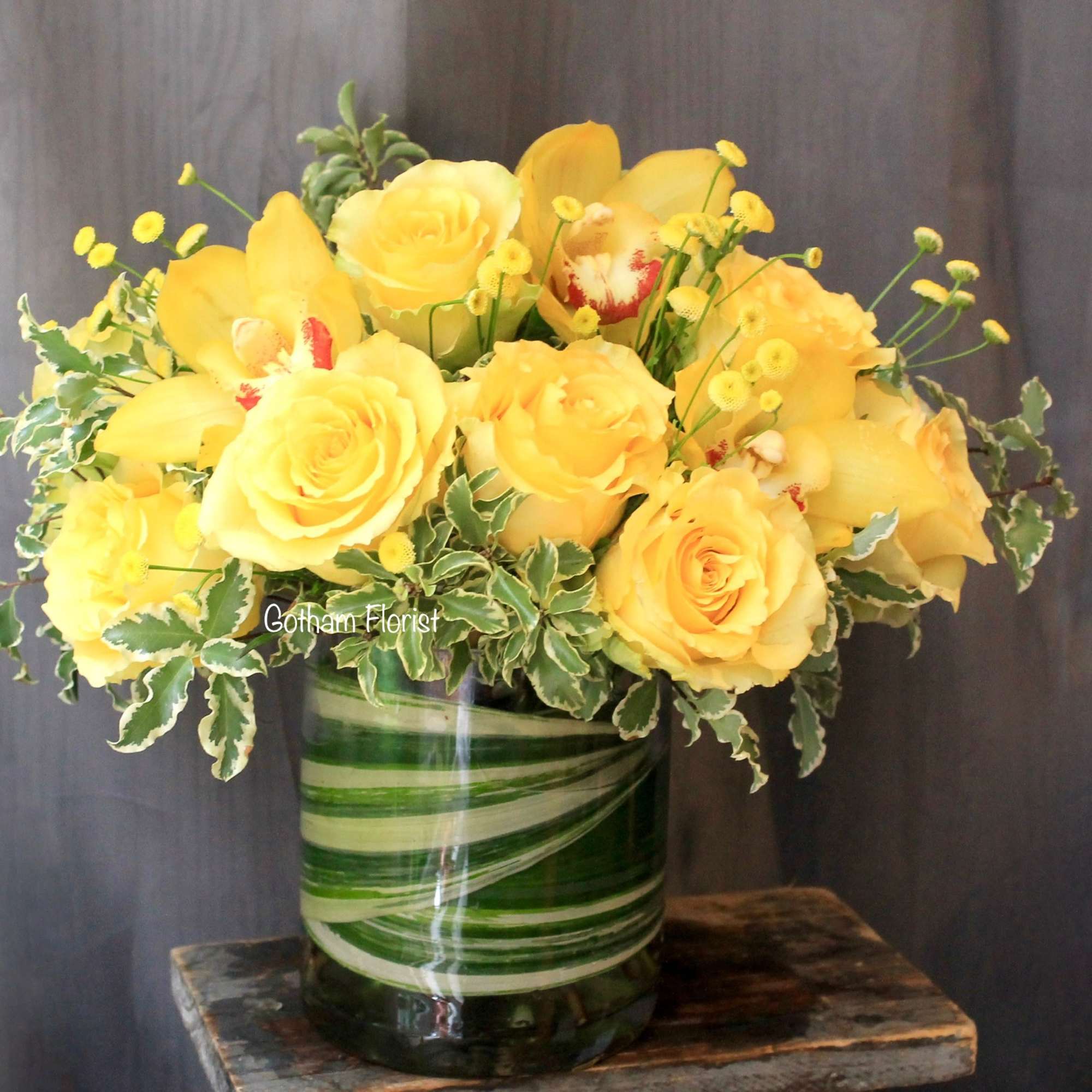 Yellow roses and orchids in a green striped glass vase