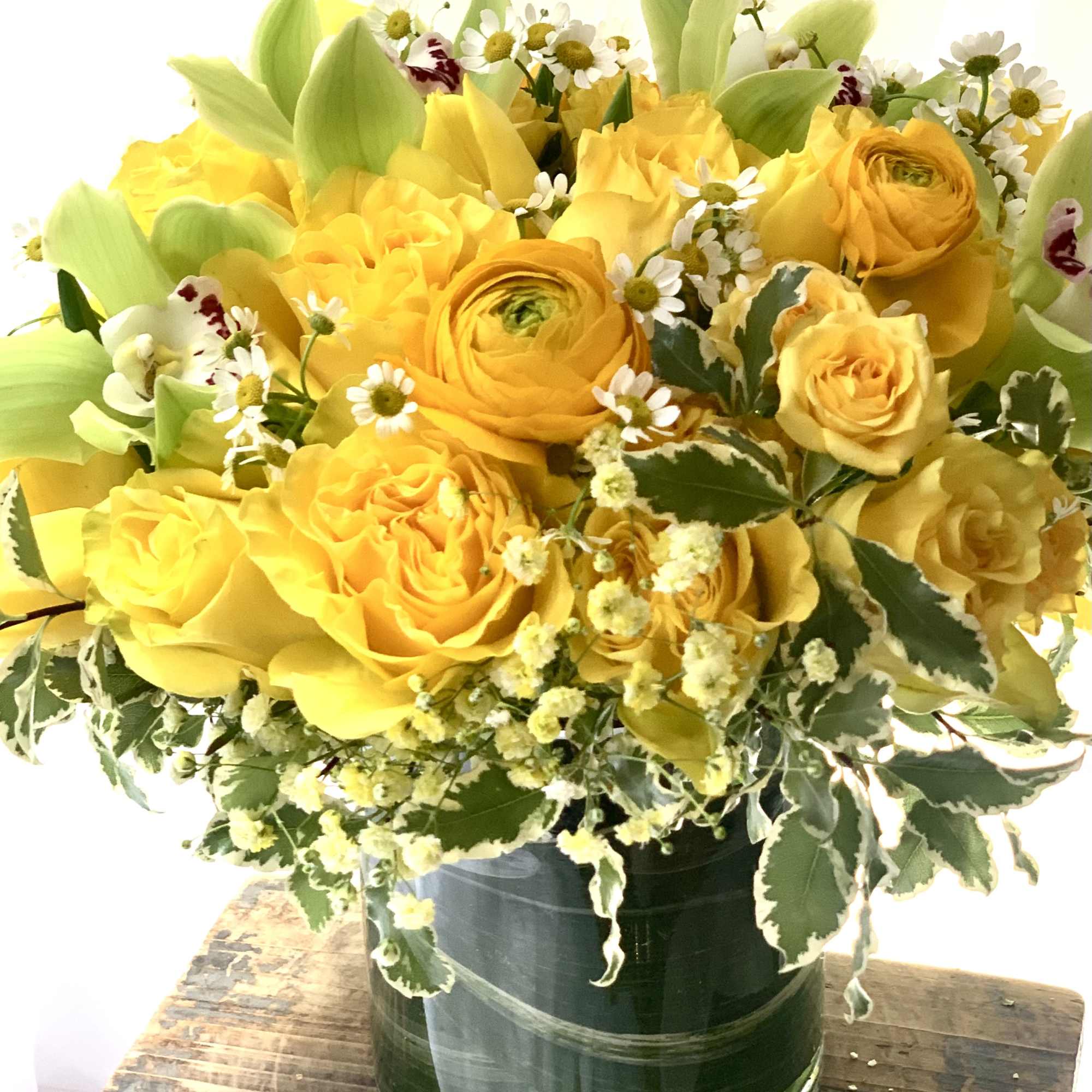 Yellow roses and ranunculus in a glass vase with small white daisies
