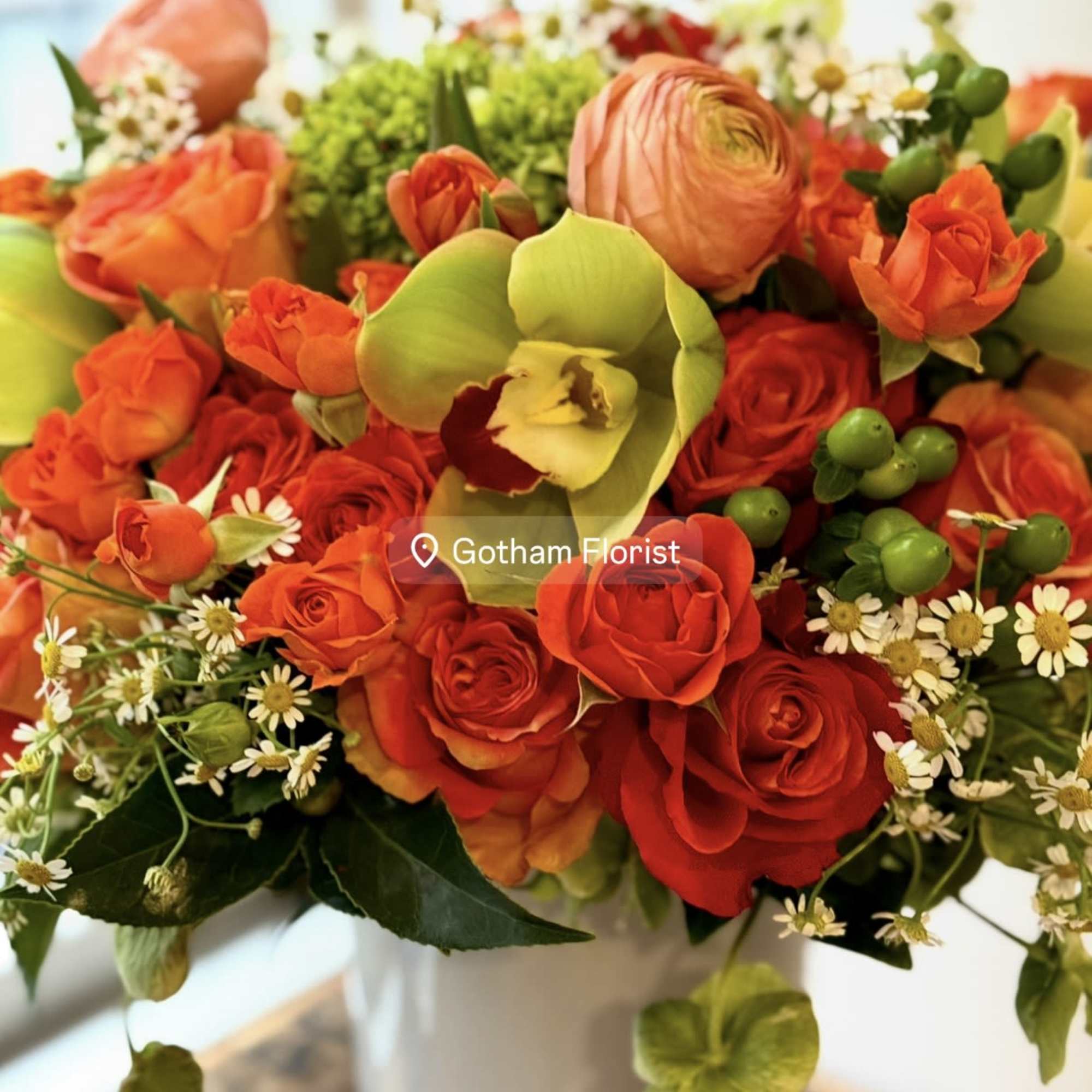 Bouquet of red and orange roses with green orchids in a white vase