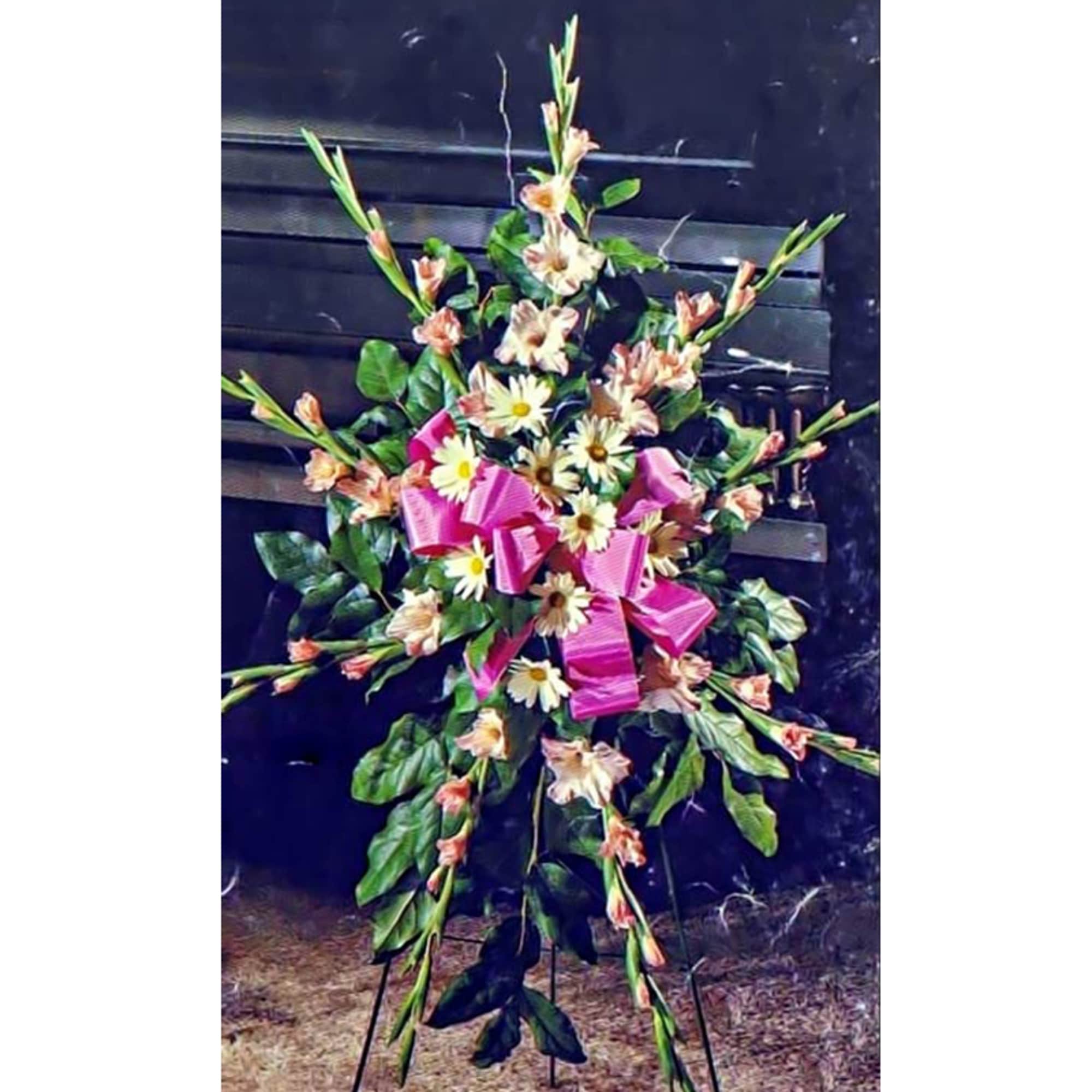 Tall standing spray of white daisies and peach flowers with a pink bow on an easel.