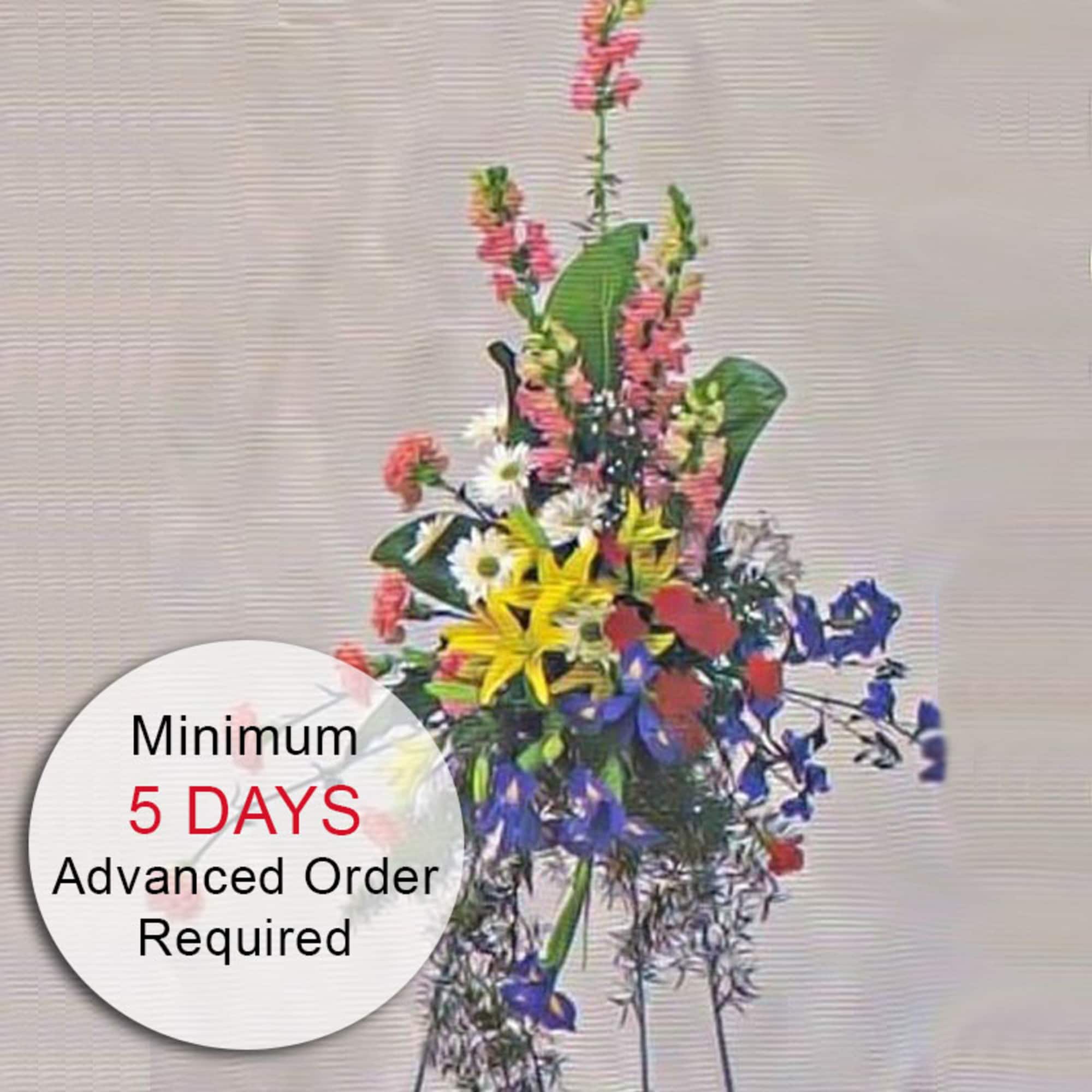 Tall multicolor standing spray with lilies, daisies, and snapdragons on an easel with a 5-day preorder message badge.