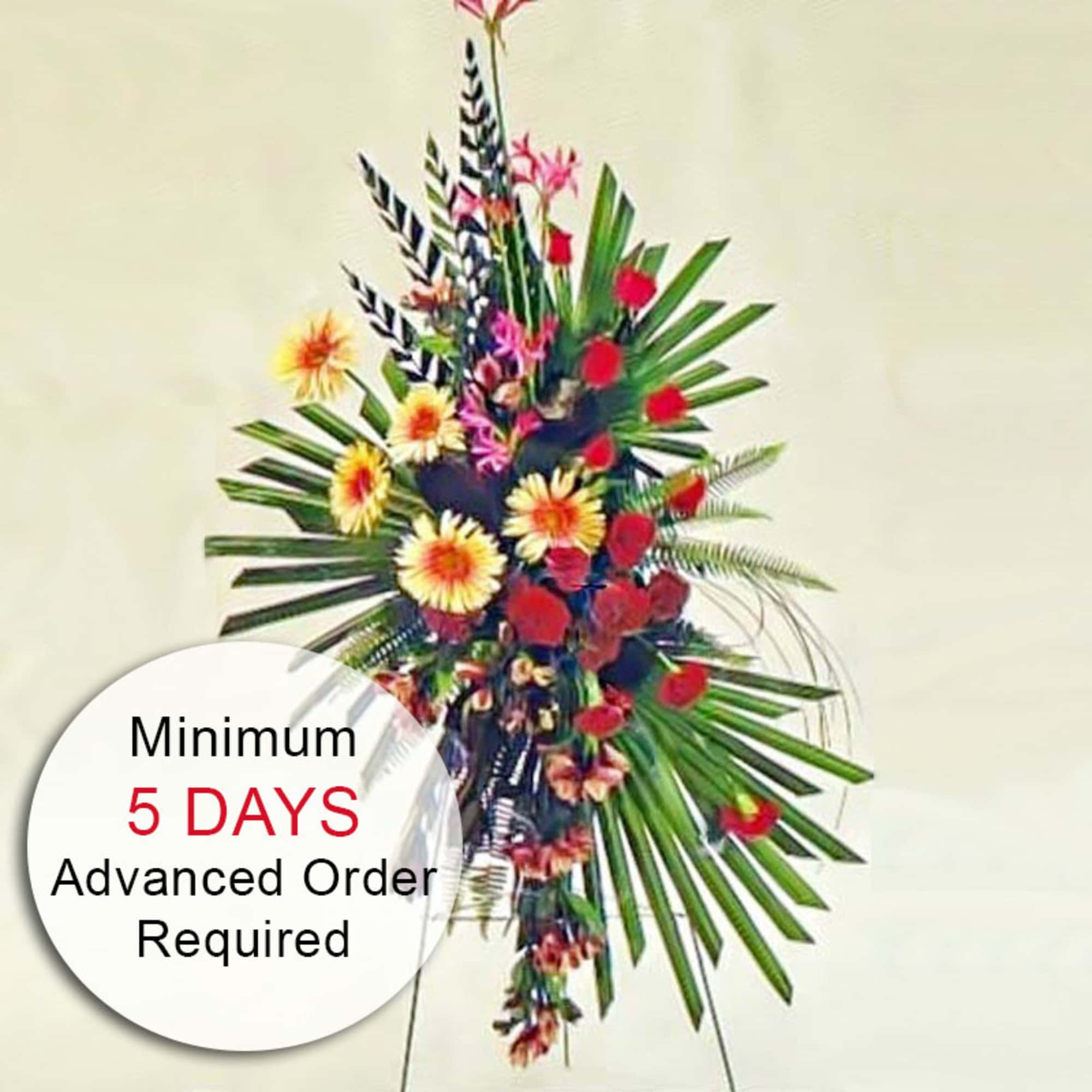 Tall standing tropical arrangement with red and yellow flowers and large palm leaves on a metal easel.