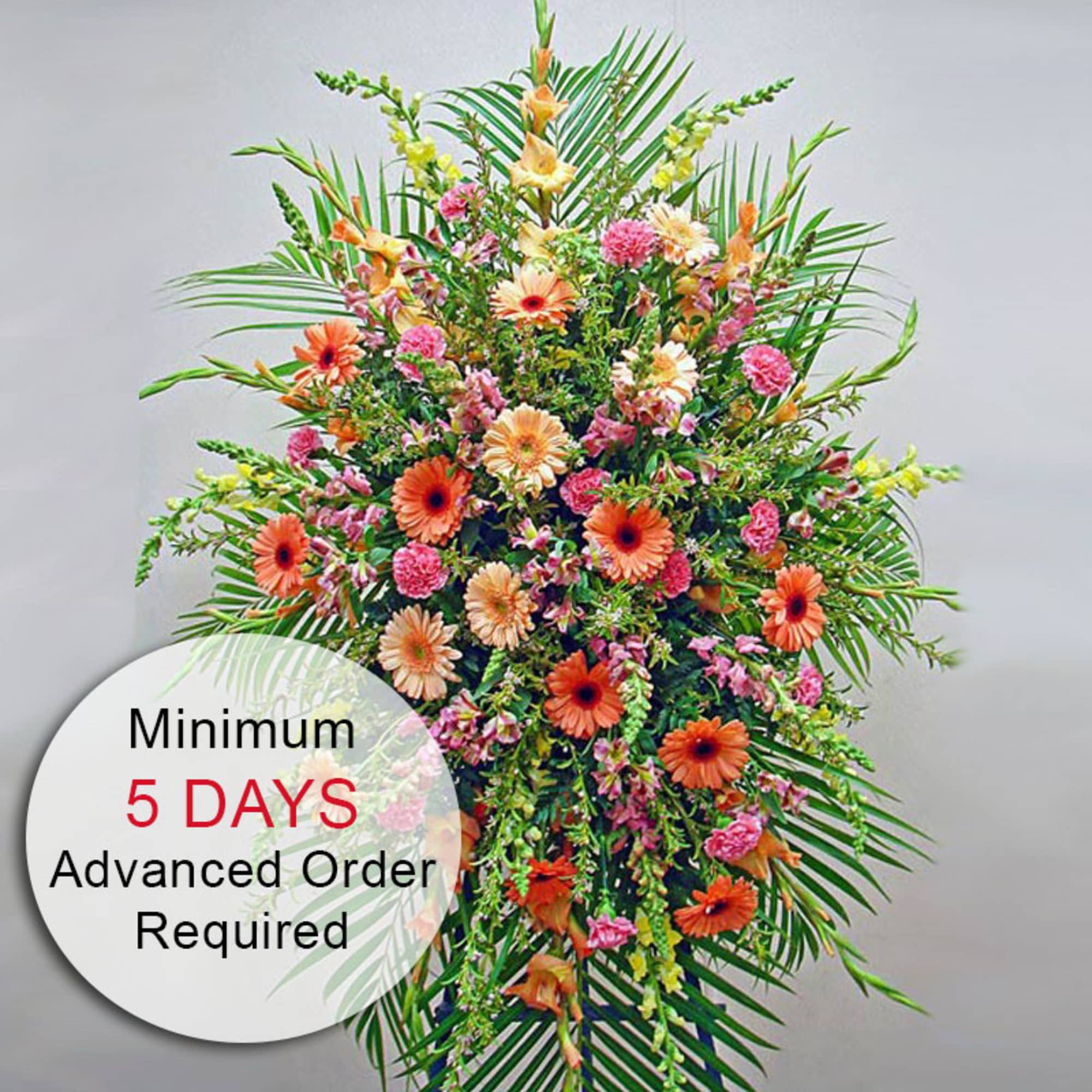 Tall standing spray of orange gerbera daisies and pink blooms with palm leaves.