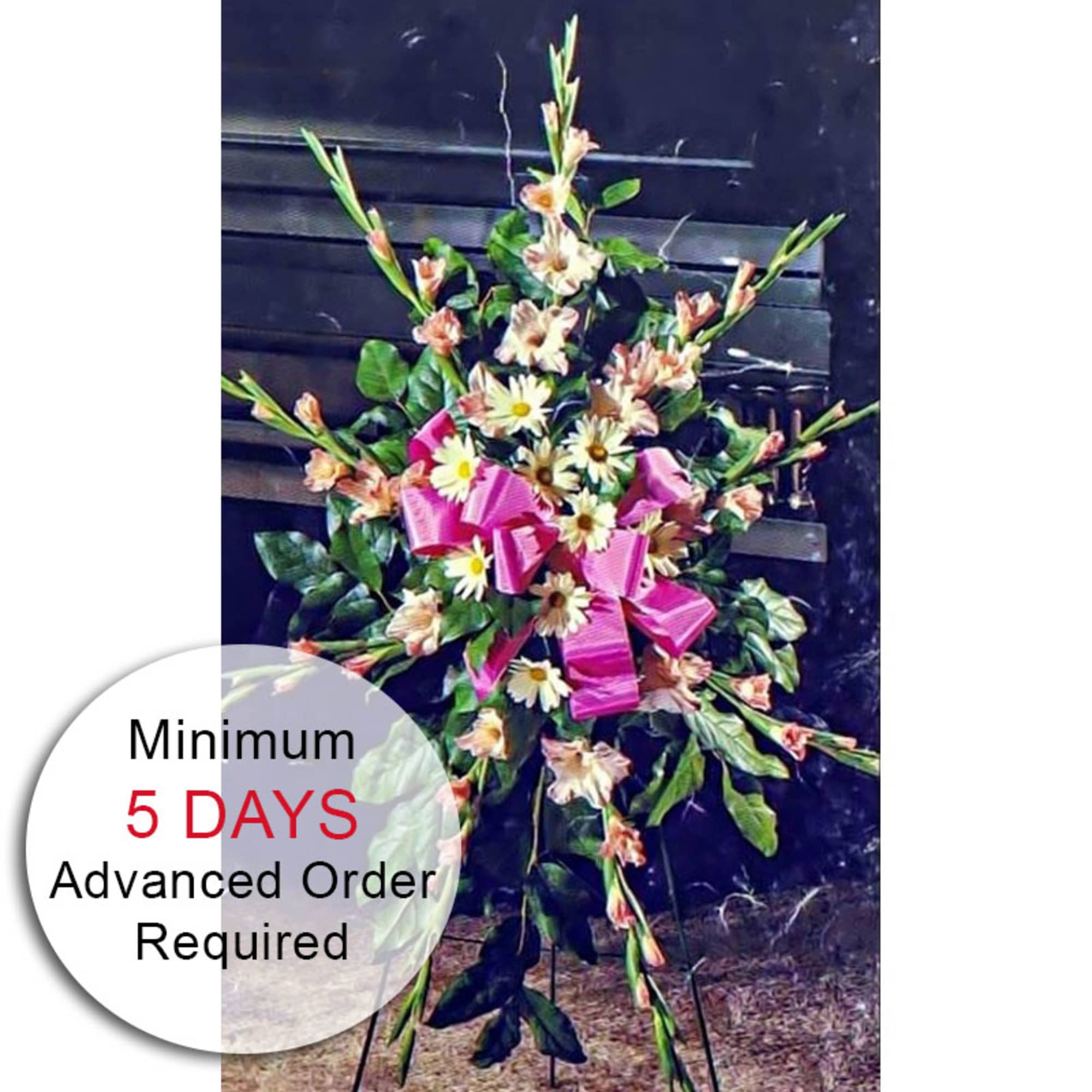 Tall standing spray with white daisies, peach flowers, and a bright pink bow on an easel.