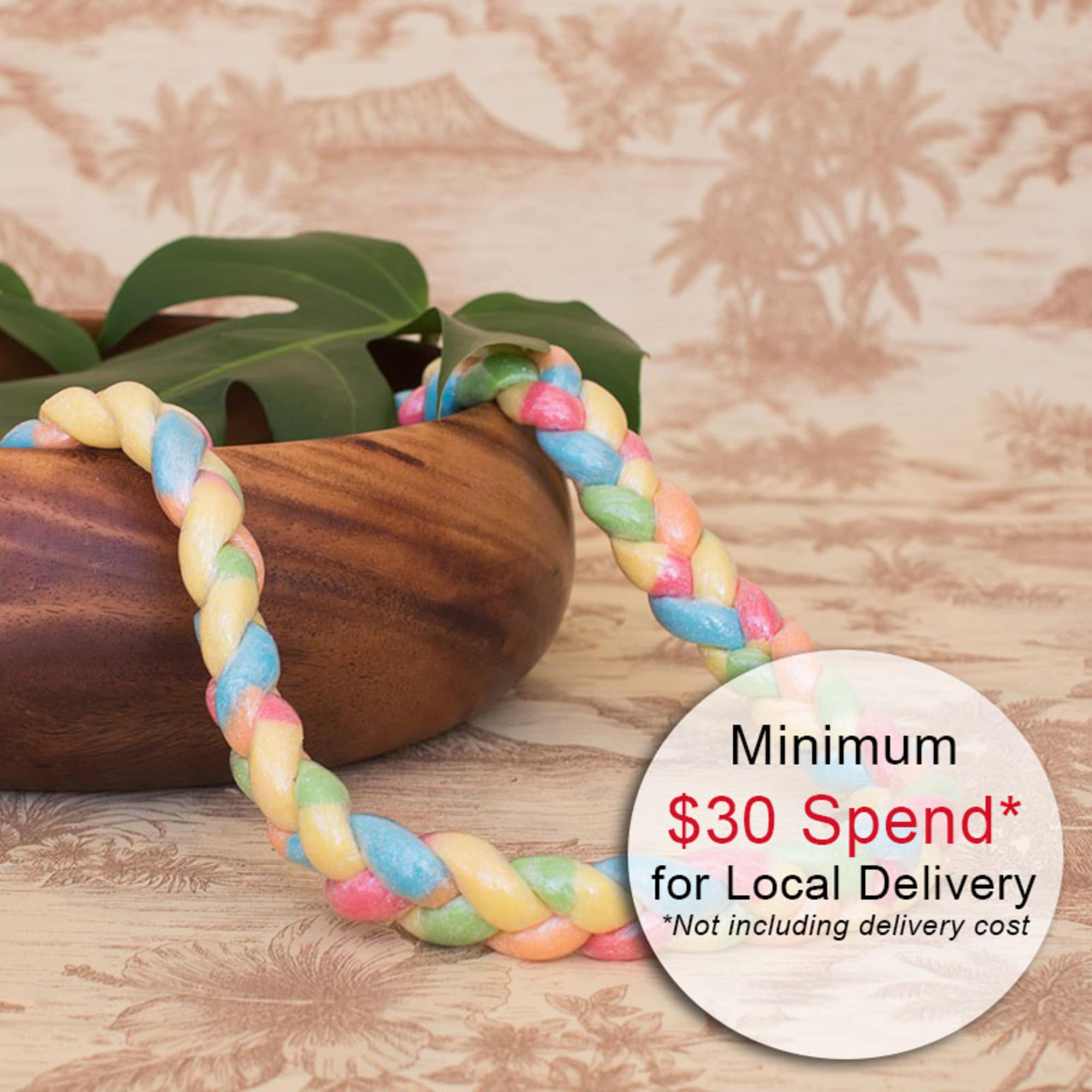 Pastel braided candy lei draped over a wooden bowl with a tropical leaf and delivery text overlay.