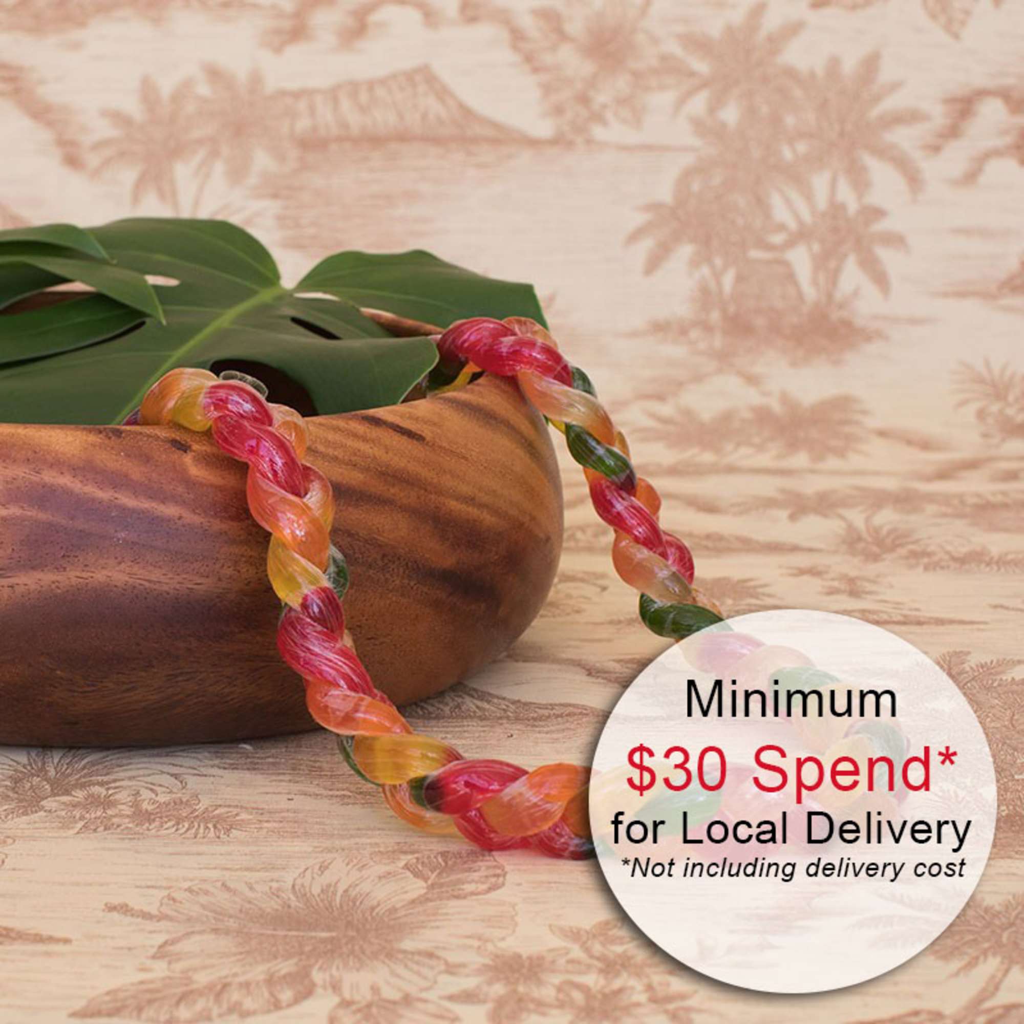 Multicolor twisted candy lei draped over a wooden bowl with a large tropical leaf