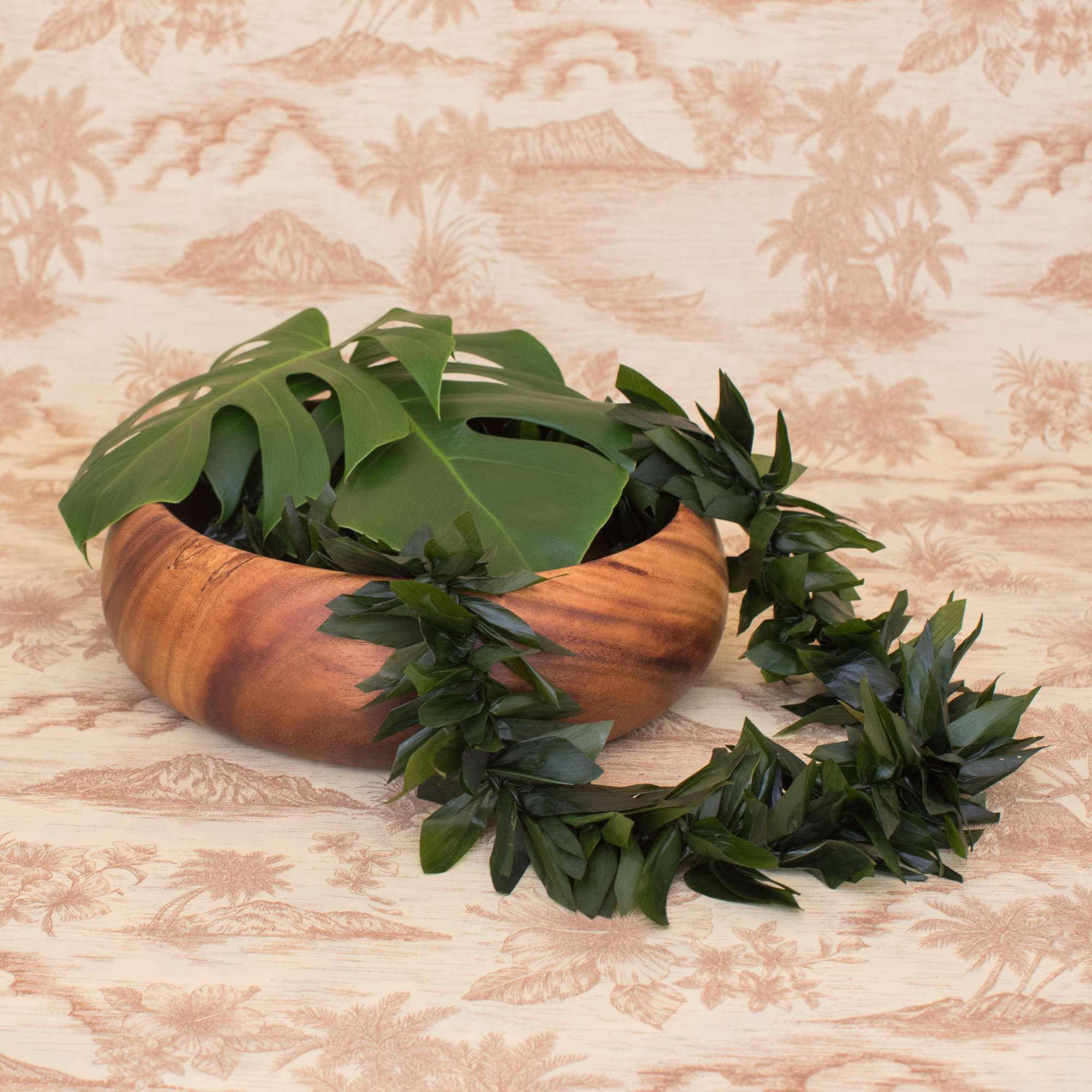 Wooden bowl with large tropical leaves and a dark green leaf lei draped over the side