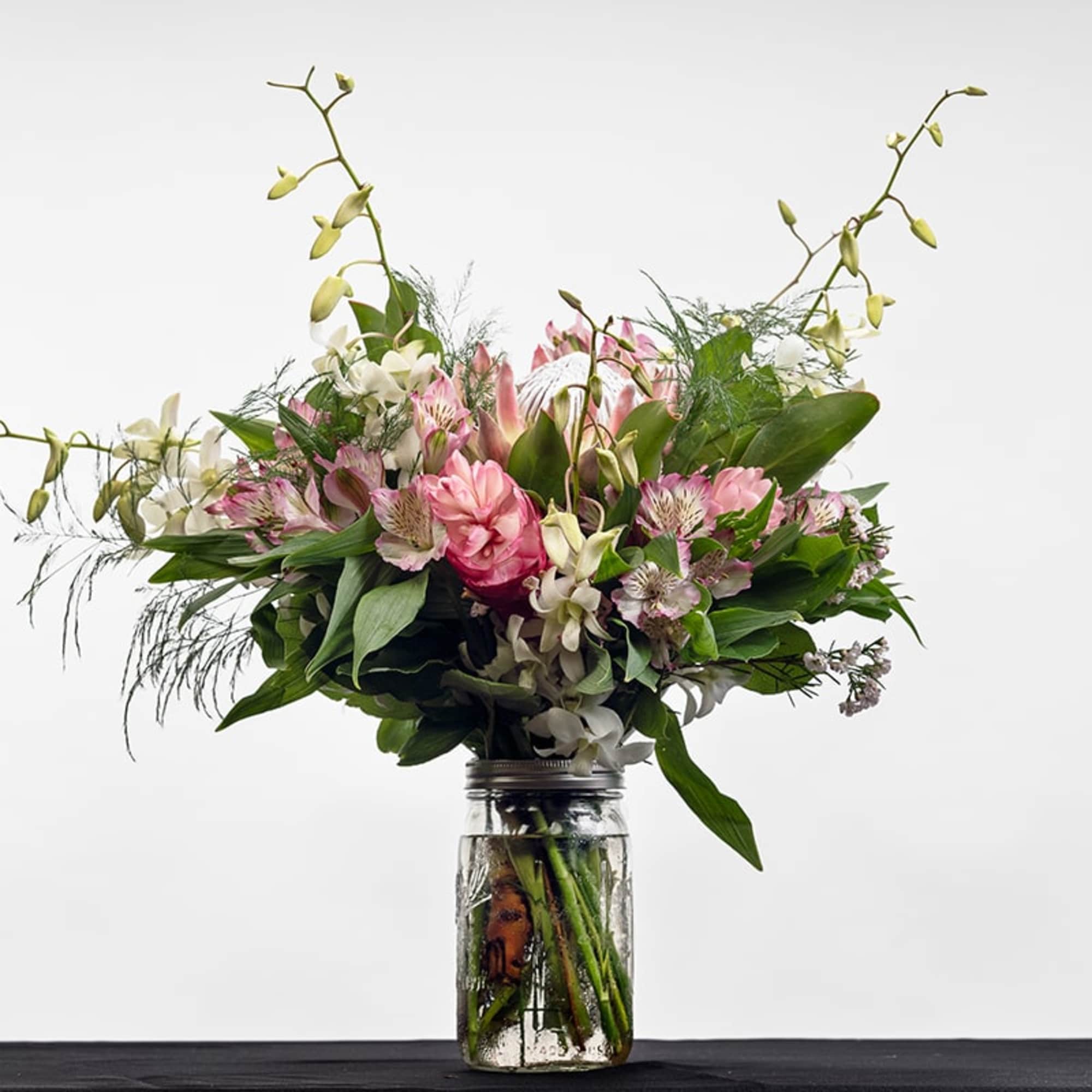 Pink and white mixed flower arrangement in a clear mason jar-style vase