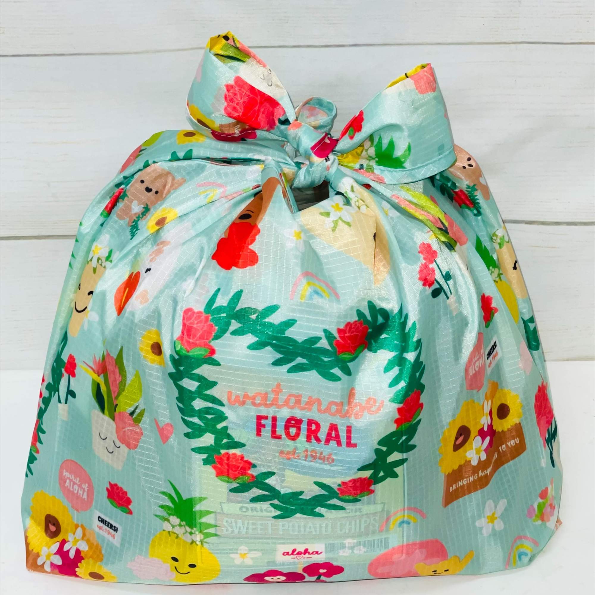 Pastel blue gift bag with colorful cartoon flowers and characters, tied at the top with a bow.