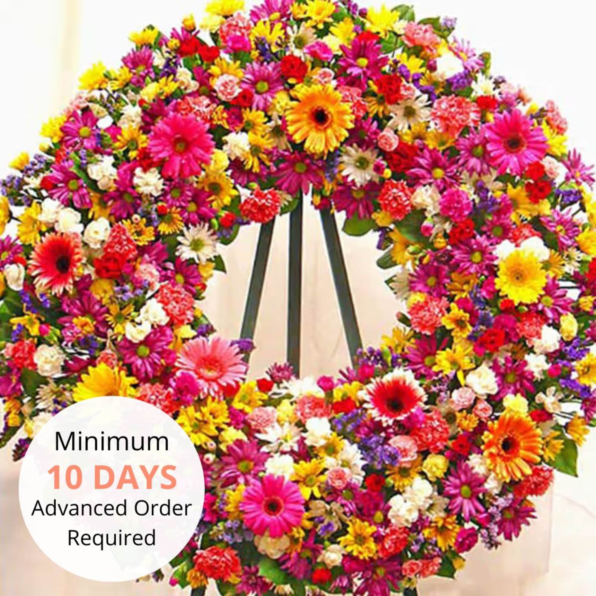 Large standing wreath of bright mixed flowers in pink, yellow, orange, and white on an easel.