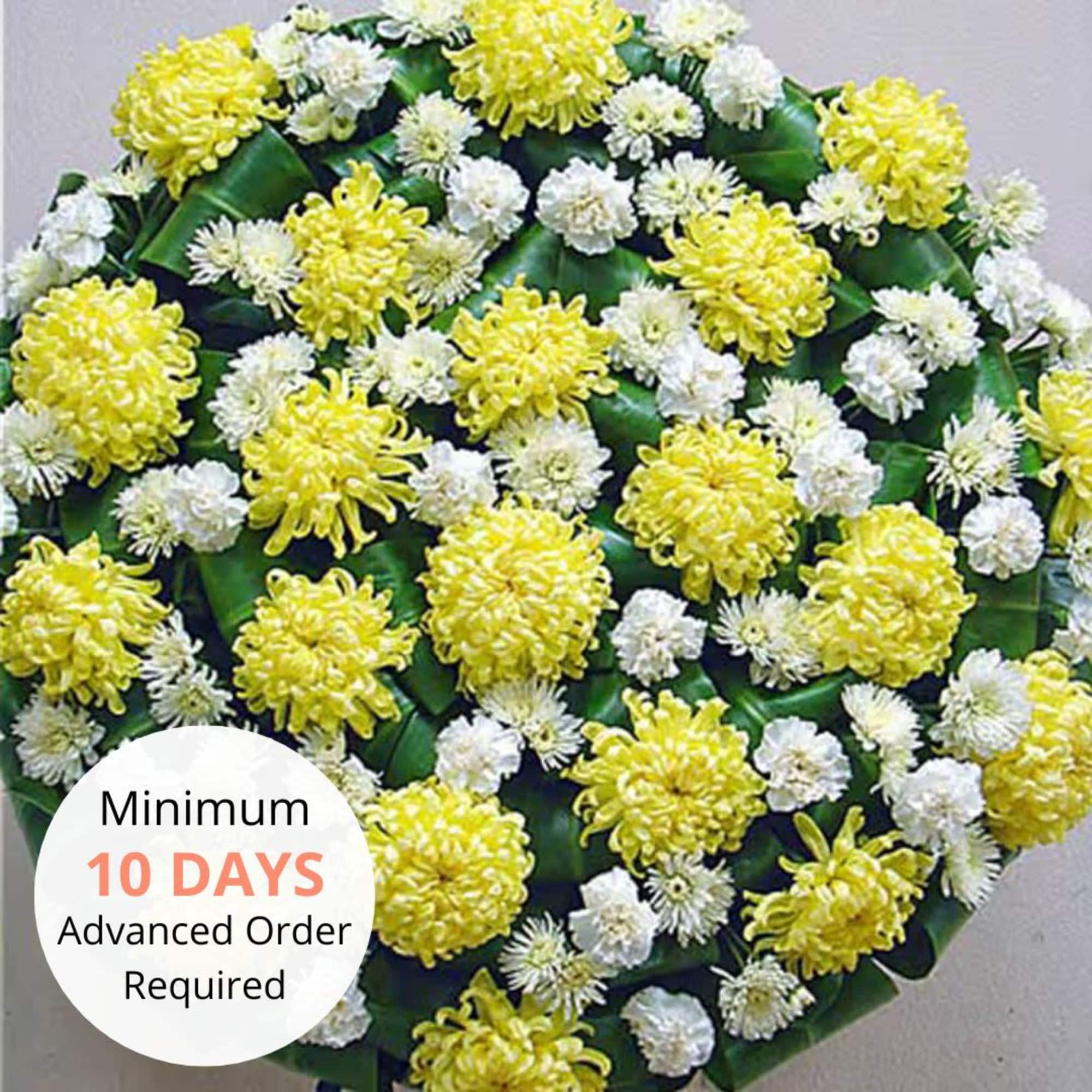Round arrangement of yellow and white chrysanthemums clustered over folded dark green leaves