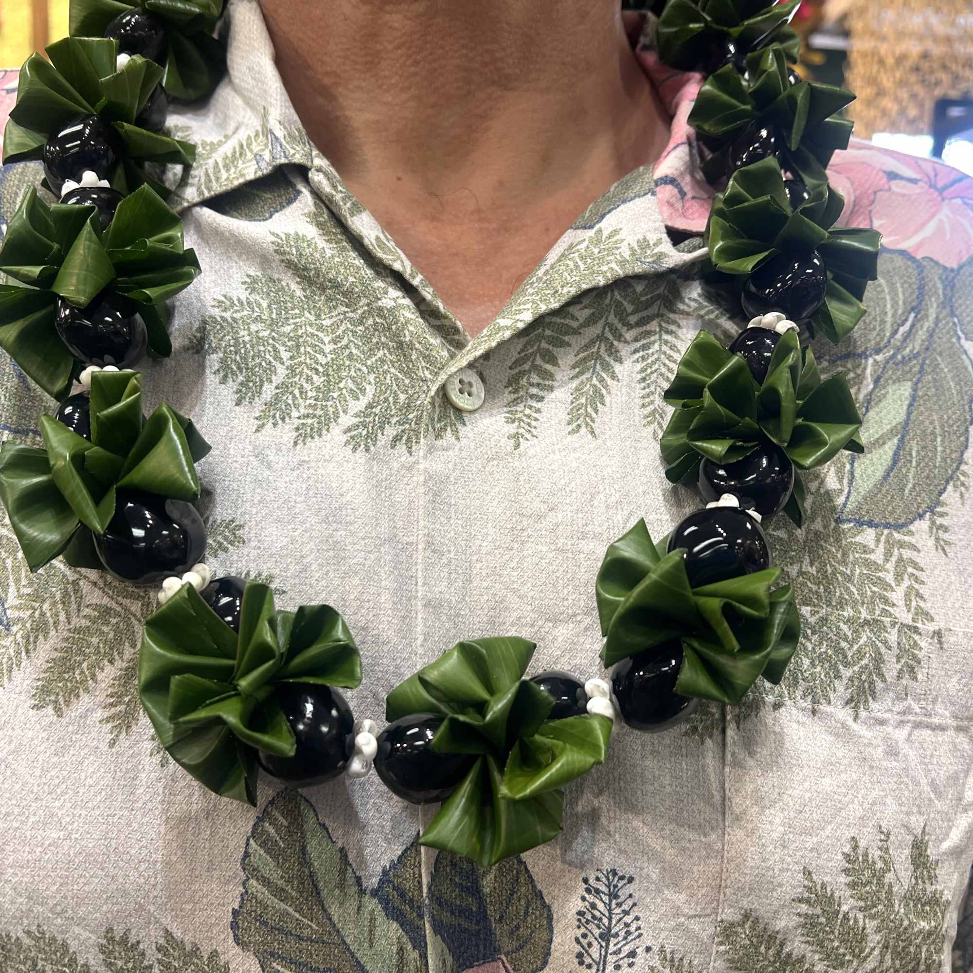 Green leaf and black bead lei necklace worn over a floral print shirt
