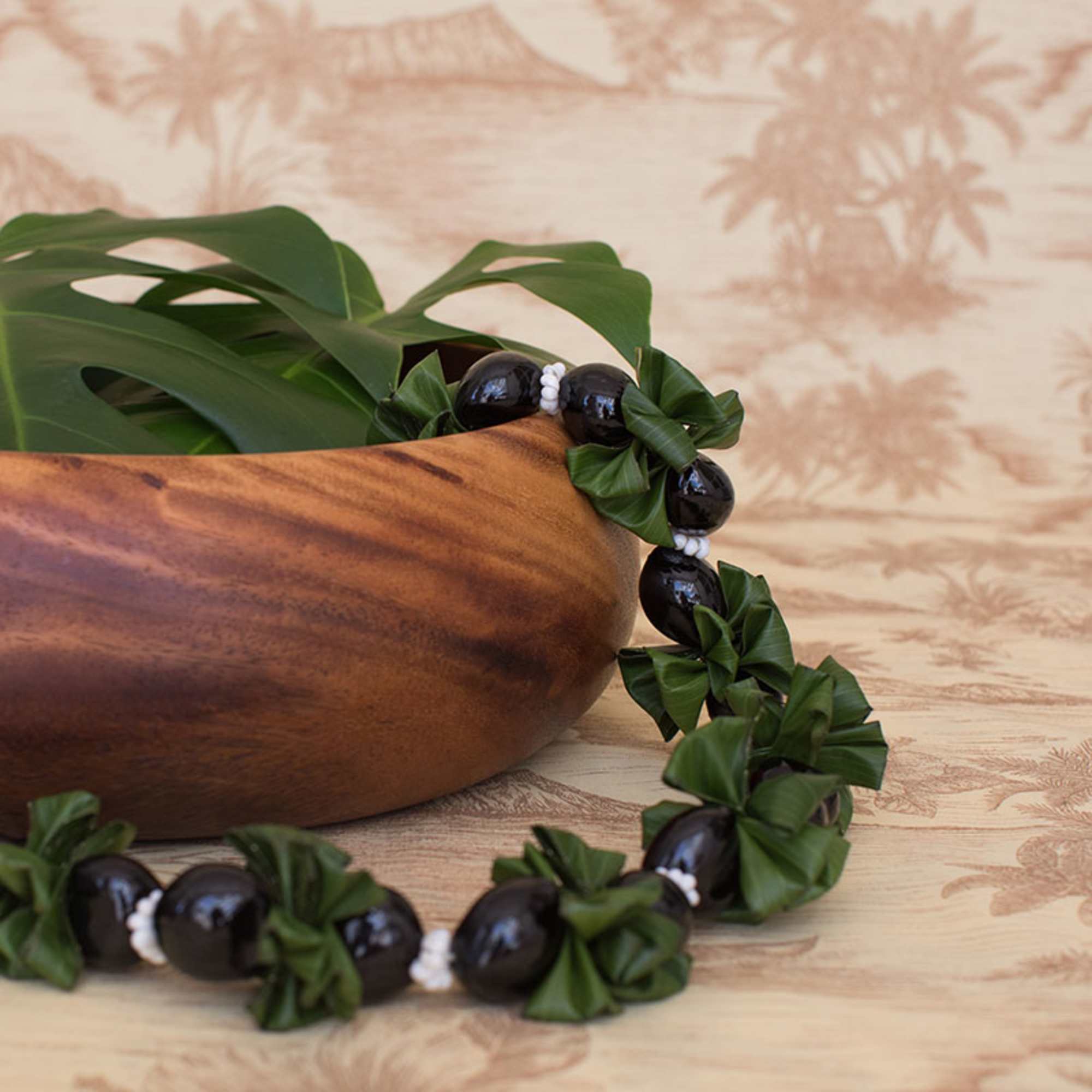 Wooden bowl with a large leaf and a black bead and green ribbon lei draped around it