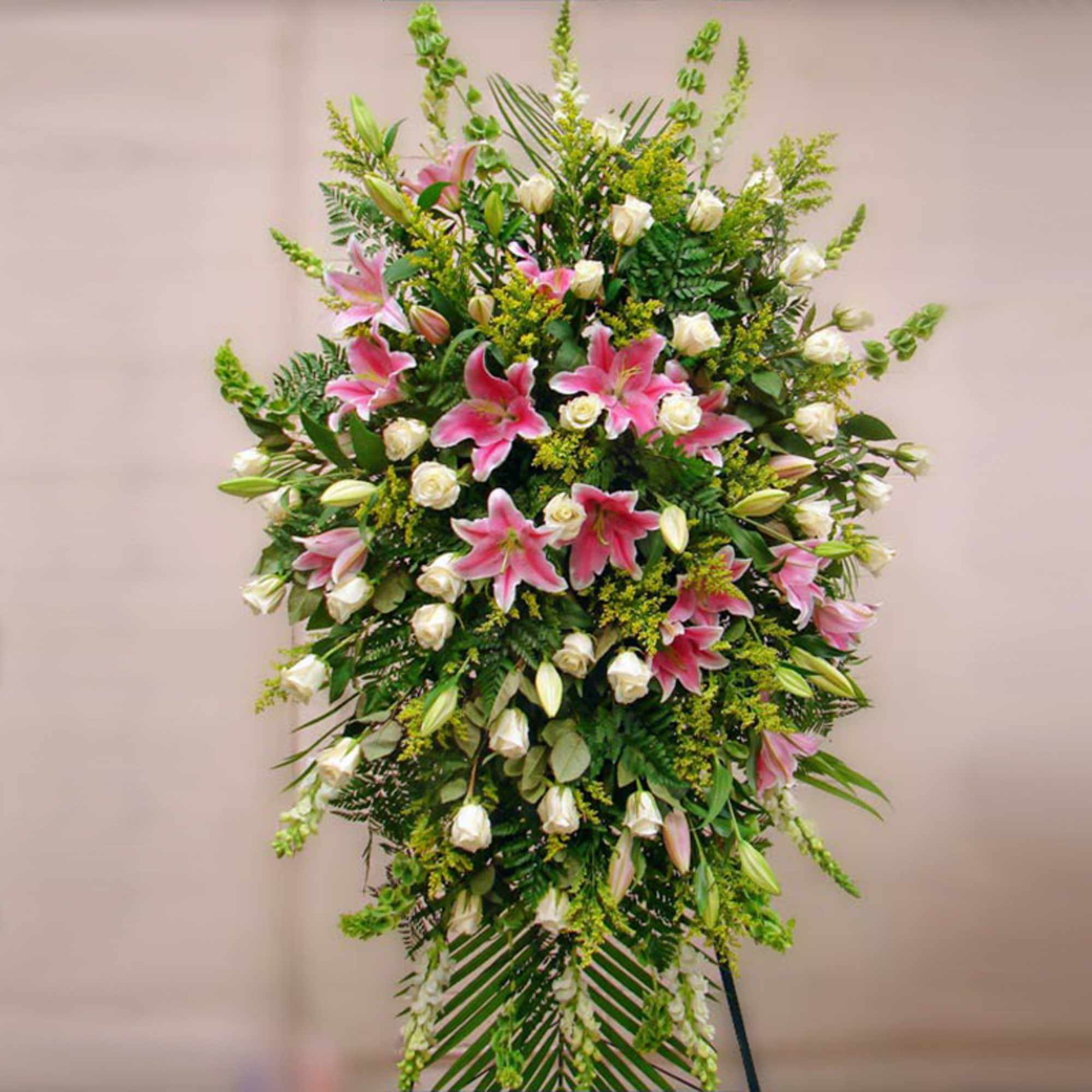 Tall standing spray with pink lilies and white roses on a green easel backdrop