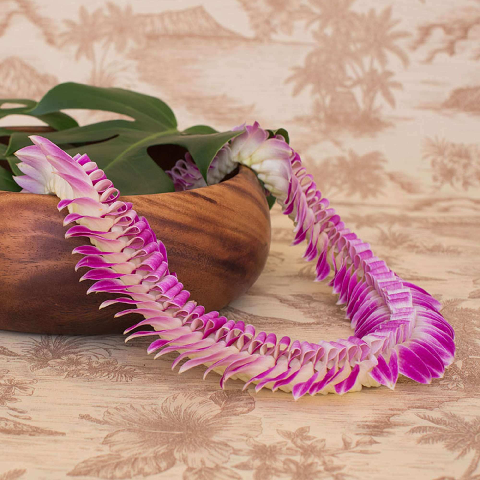 Purple and white orchid lei draped over a wooden bowl