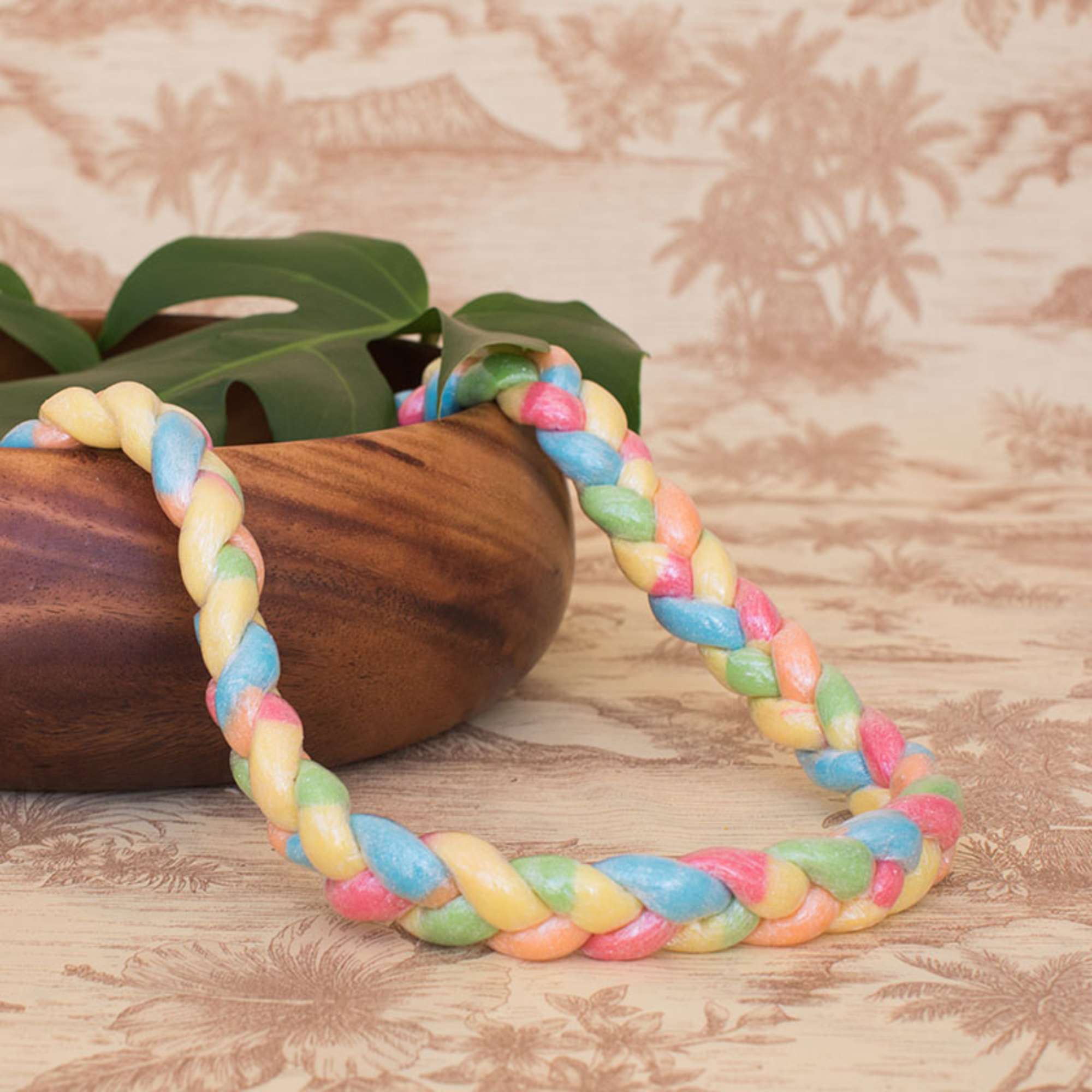 Braided pastel lei necklace in yellow, blue, pink, and green resting on a wooden bowl