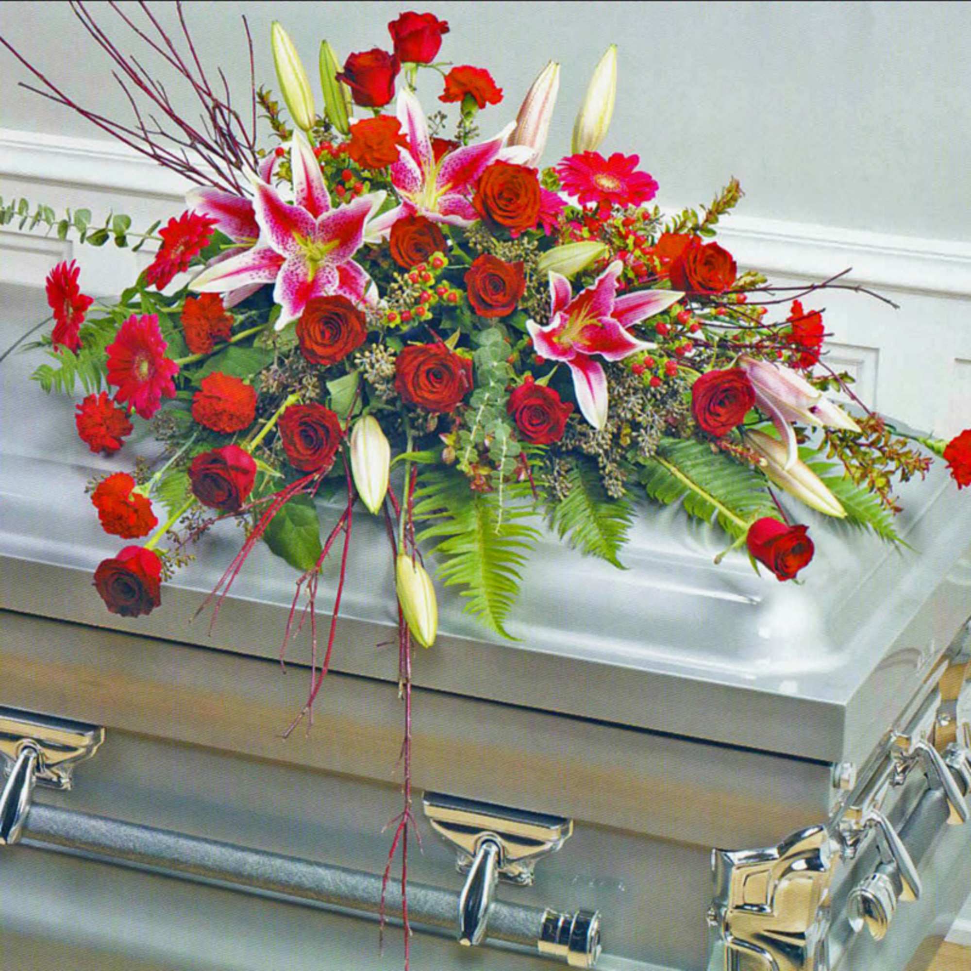 Red and pink floral casket spray with lilies and roses on a silver casket