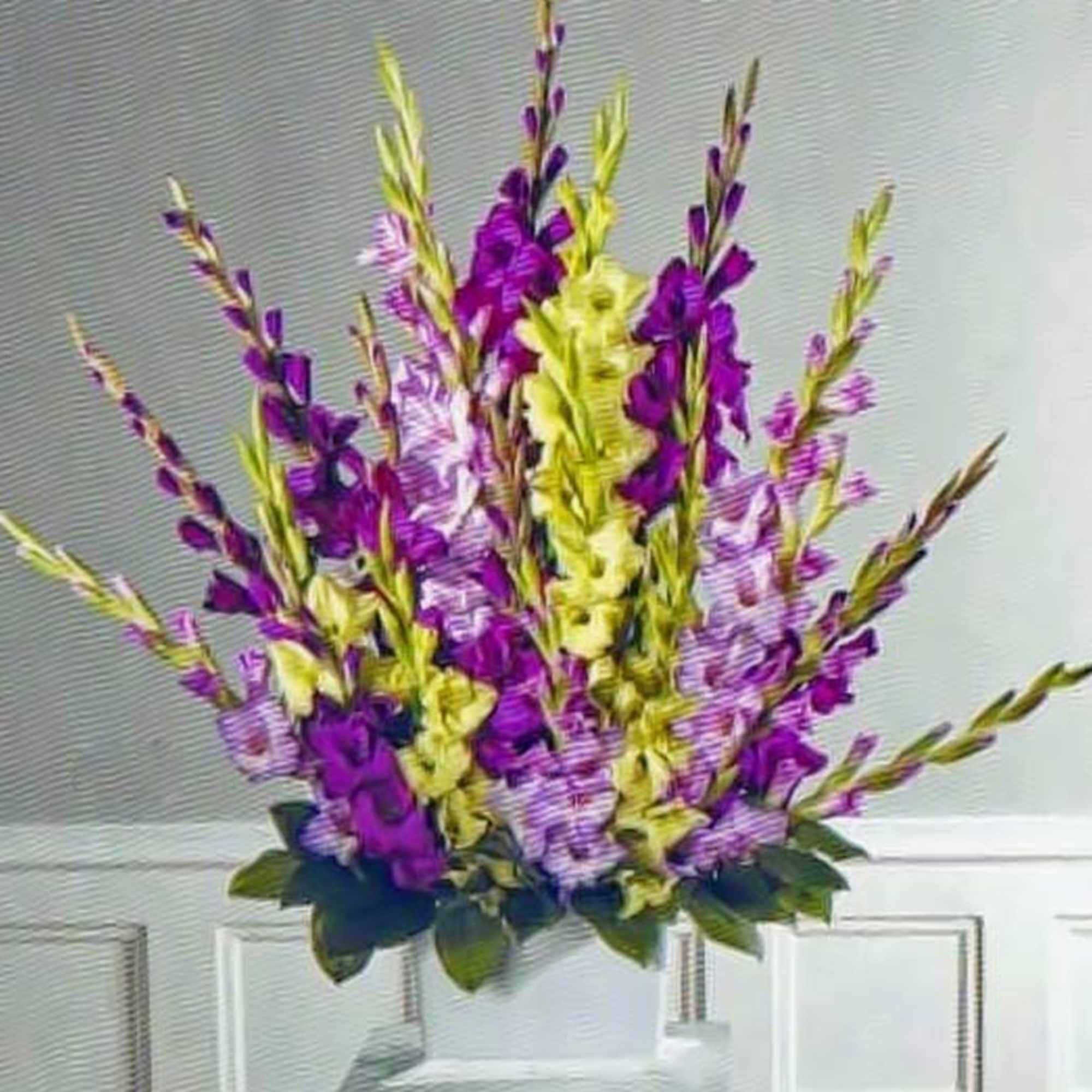 Tall arrangement of purple and pale yellow flowers in a white pedestal vase