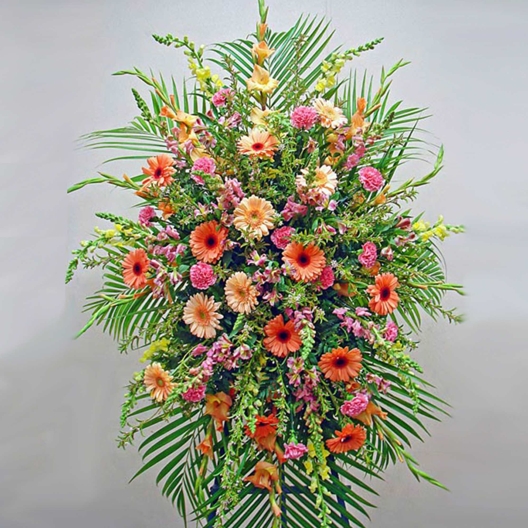 Tall standing spray of orange gerbera daisies and pink flowers framed by palm fronds