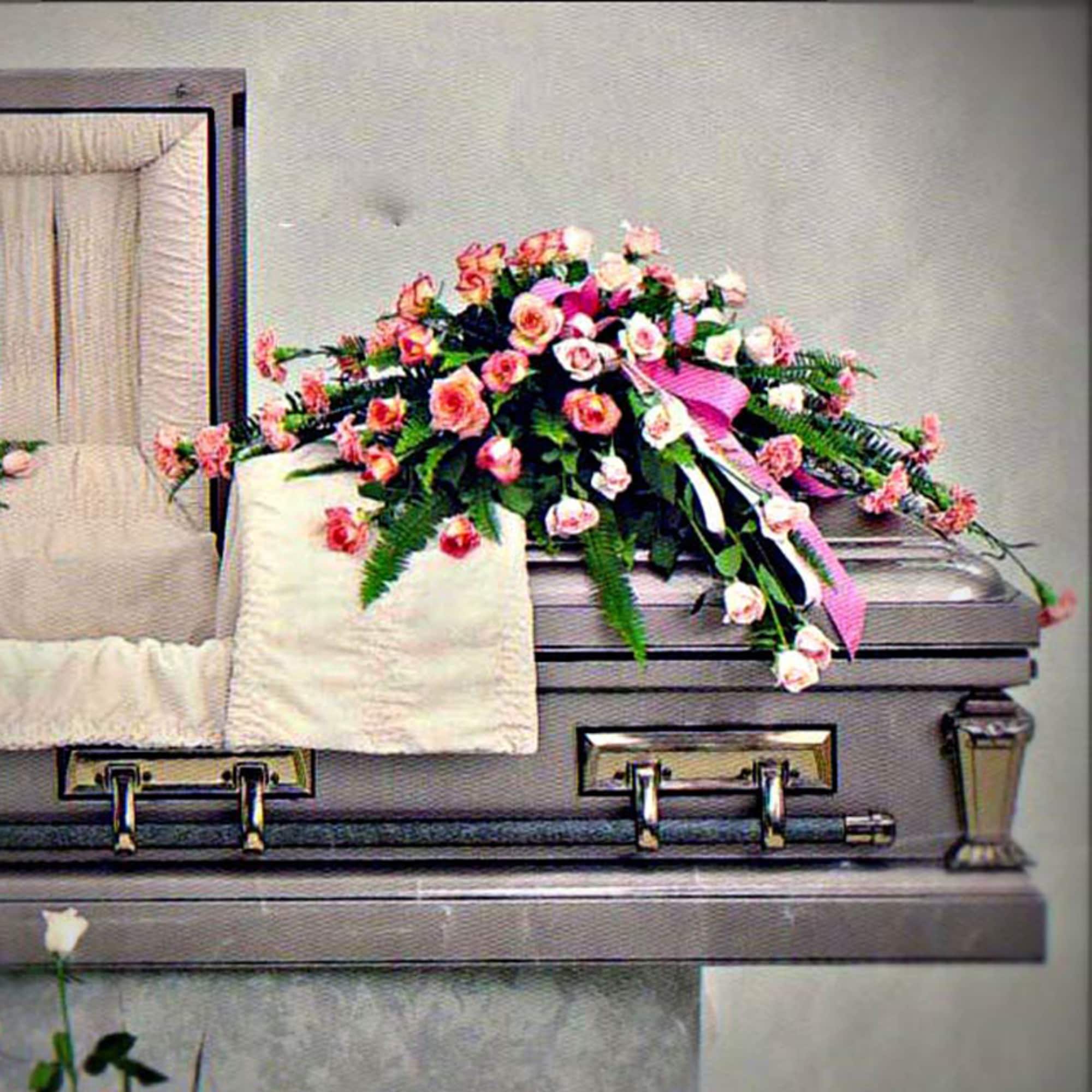 Pink rose casket spray with ribbon displayed on an open silver casket