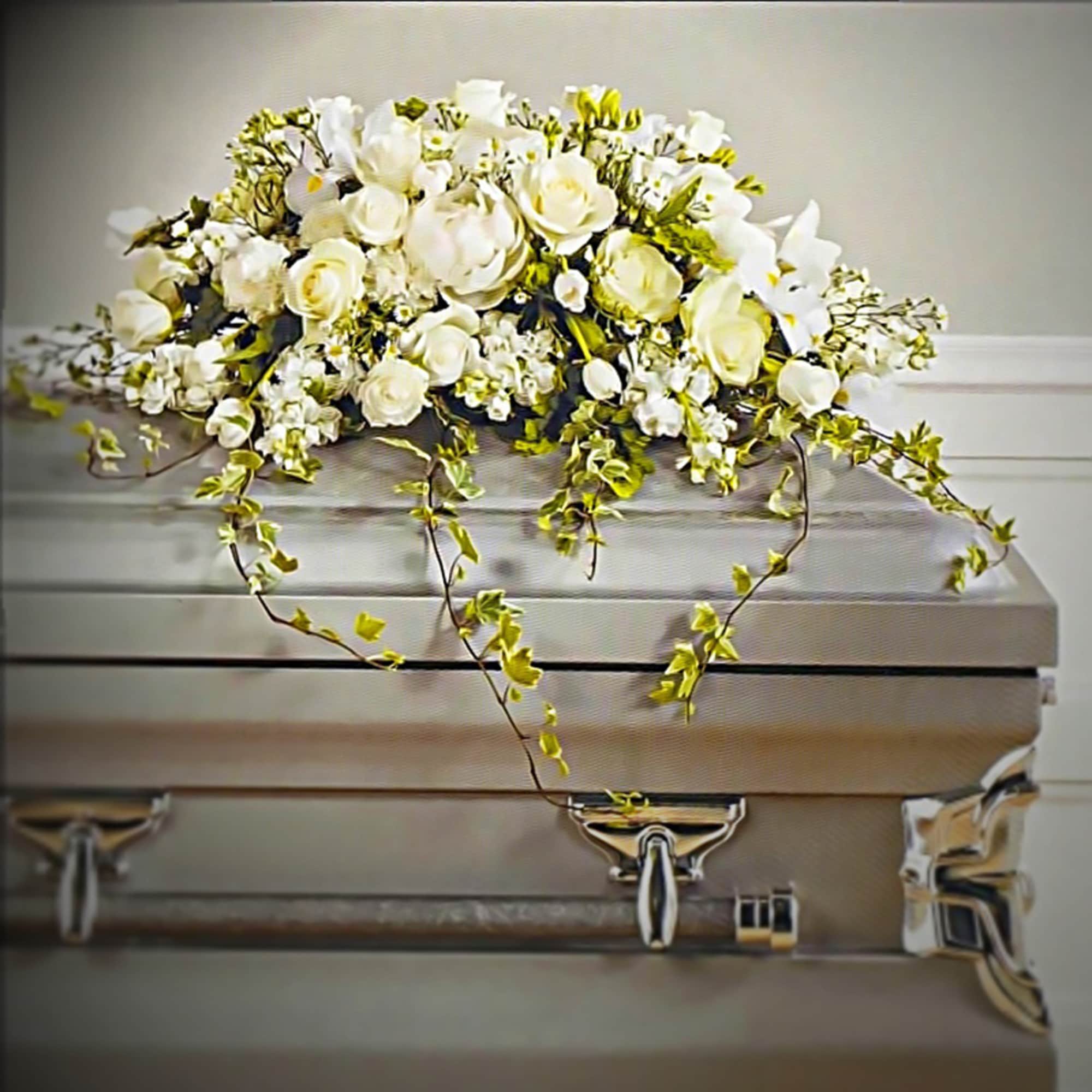 White floral casket spray with trailing greenery on a silver casket