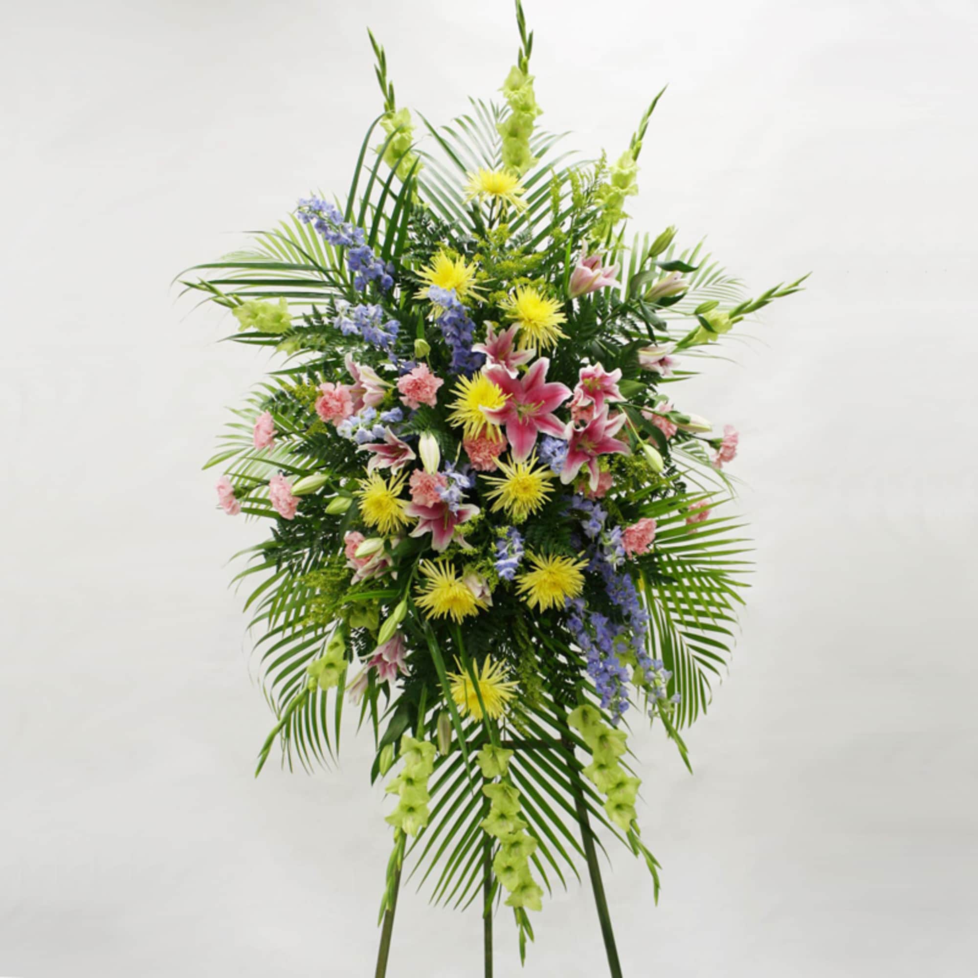 Tall standing spray with pink lilies, yellow mums, and mixed flowers on a green easel
