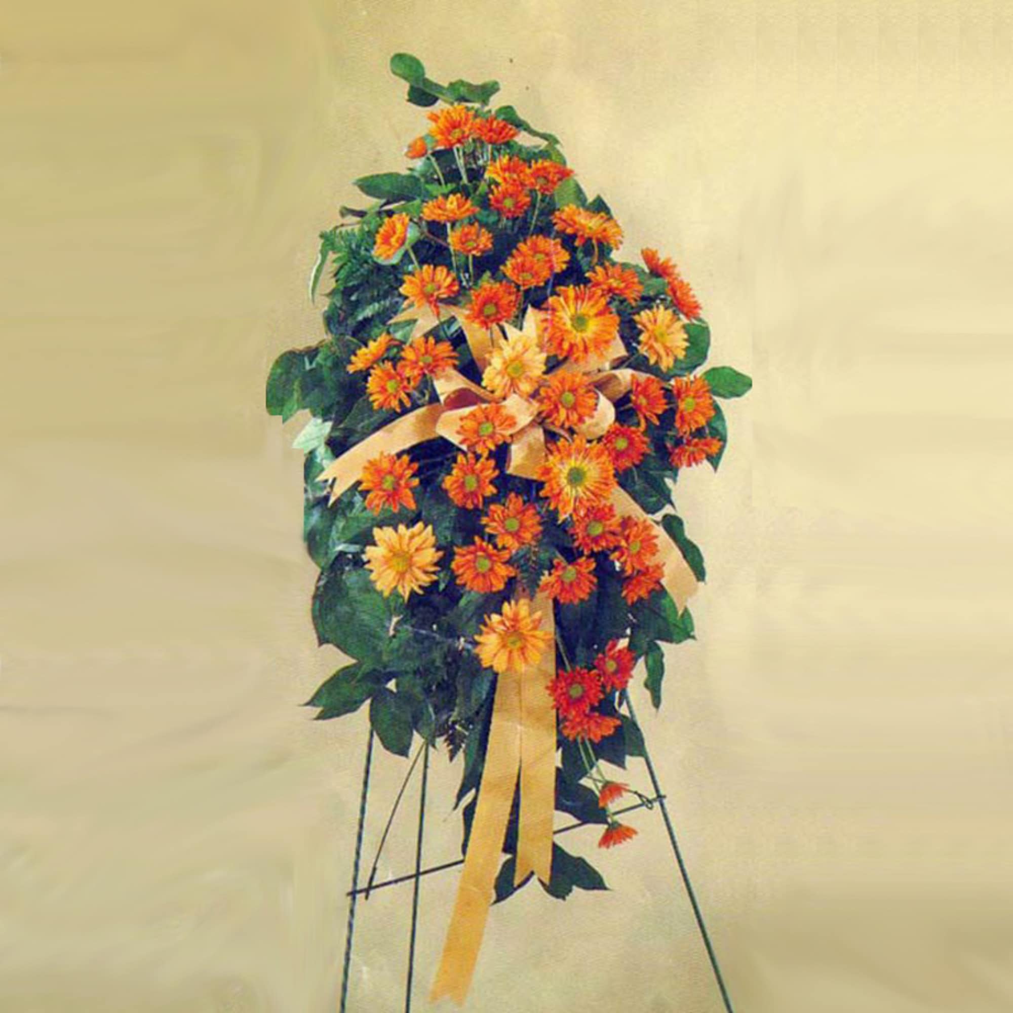 Tall standing spray of orange gerbera daisies with yellow ribbon and greenery on an easel
