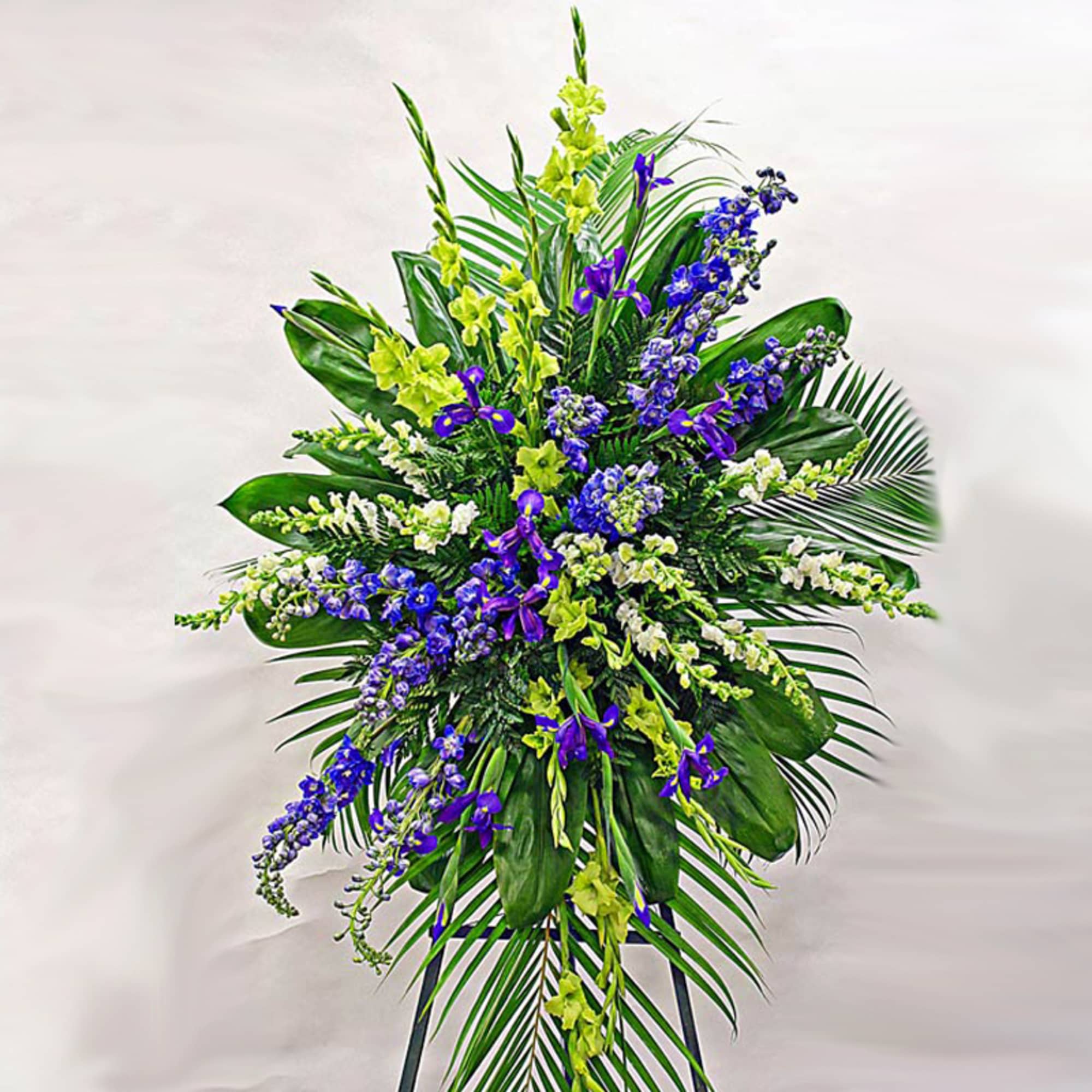 Tall standing spray of purple and white flowers with yellow accents and large palm leaves on an easel