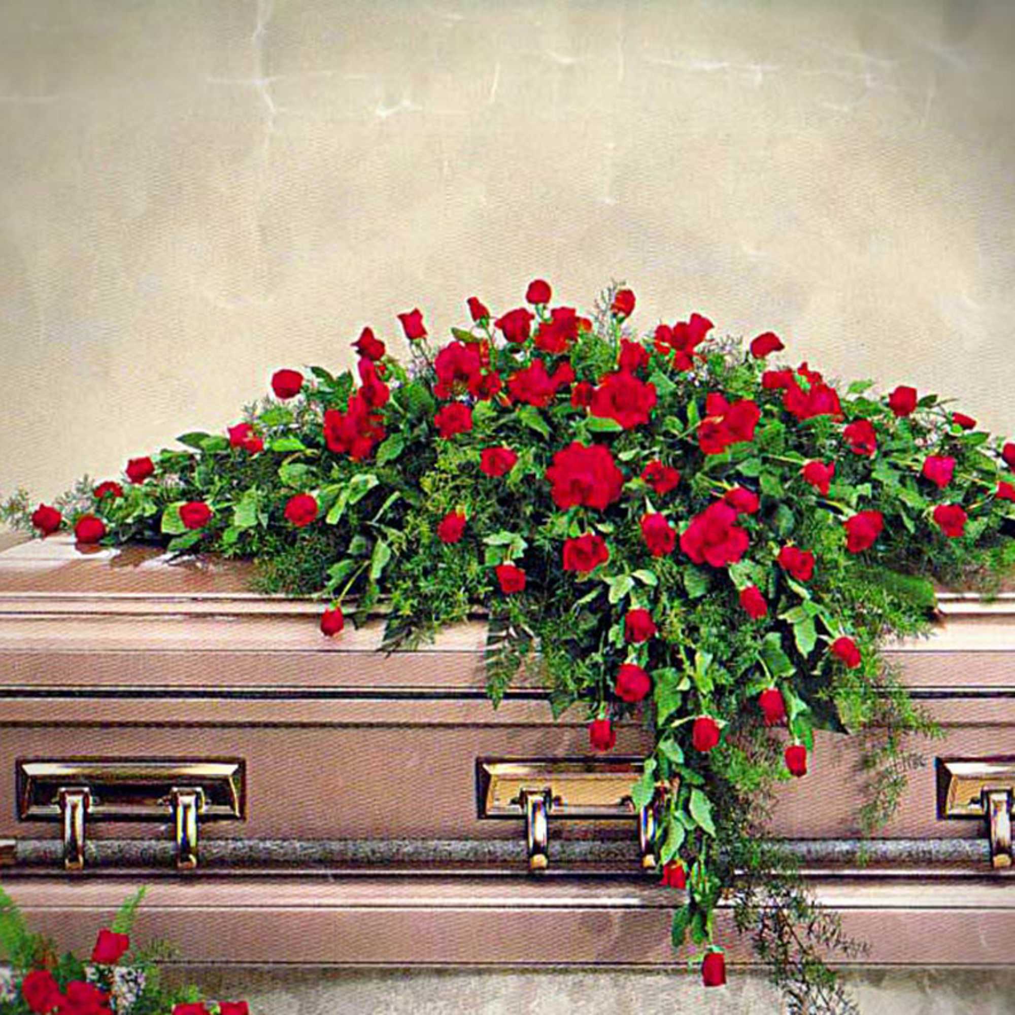 Casket spray of red roses and lush greenery on a bronze casket.