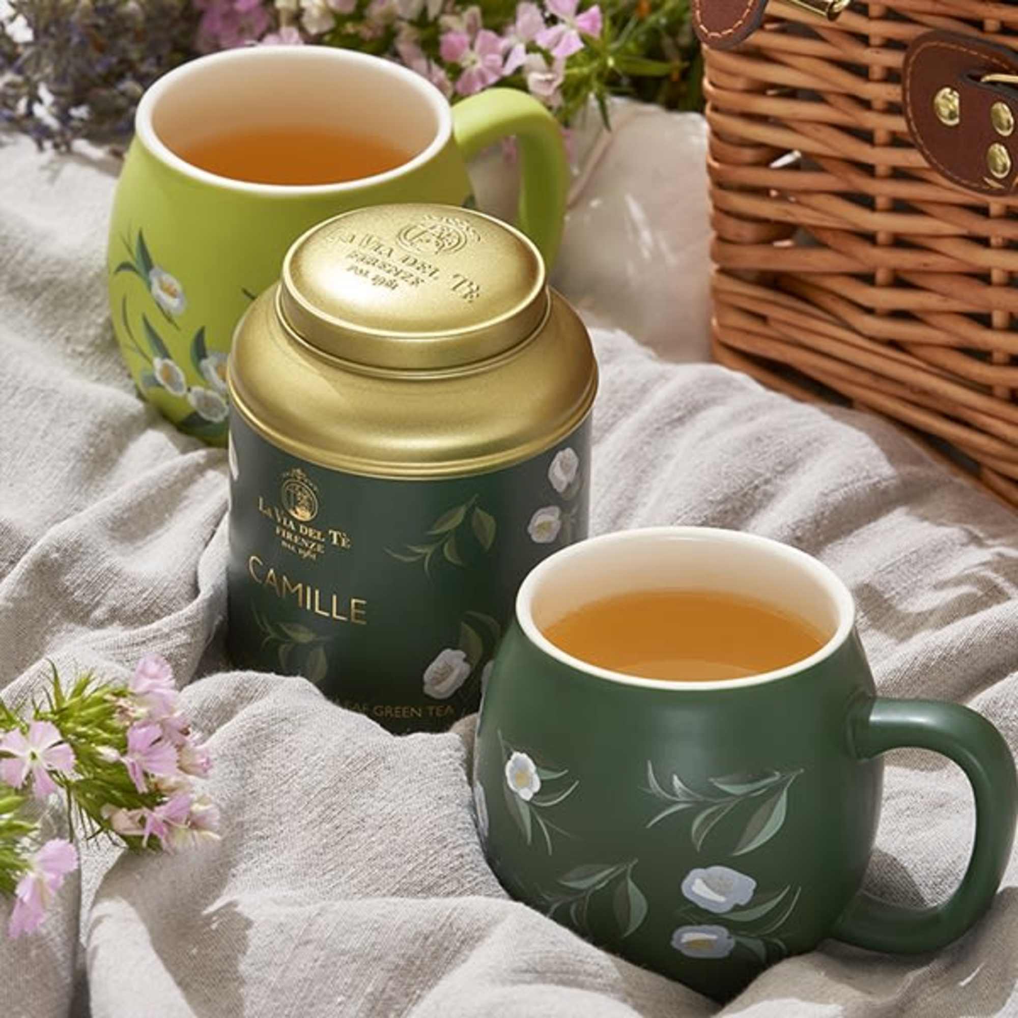 Two green floral mugs and a camomile tea tin on a cloth.