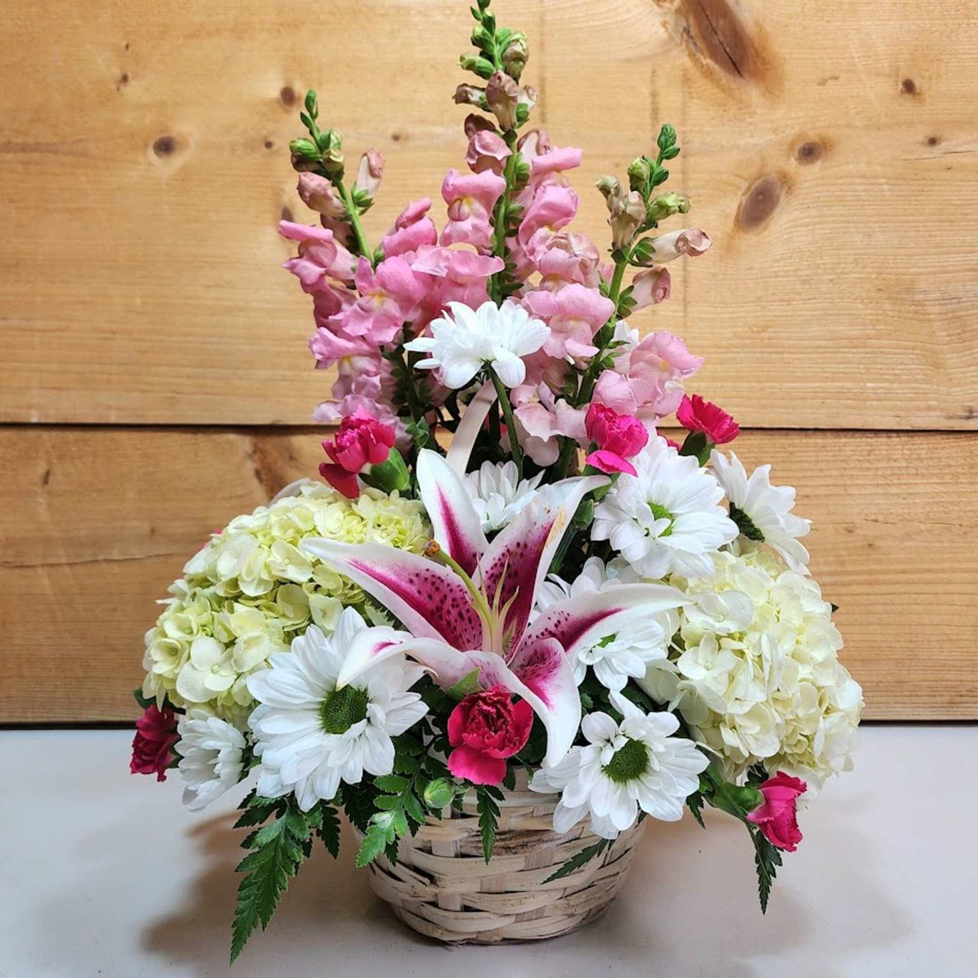 Basket arrangement with pink snapdragons, white daisies, lilies, and pale hydrangeas