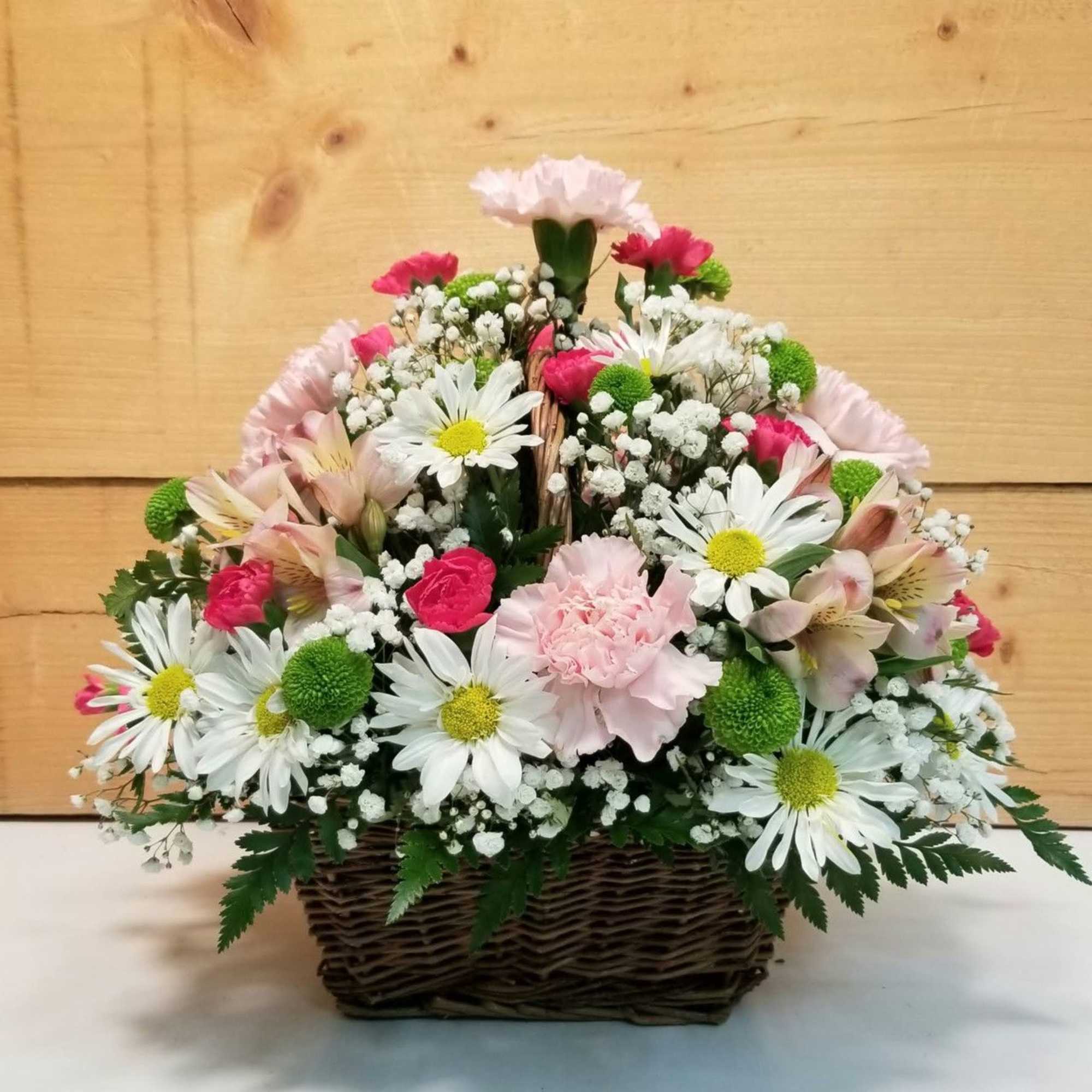 Wicker basket arrangement with white daisies, pink carnations, and mixed pastel flowers