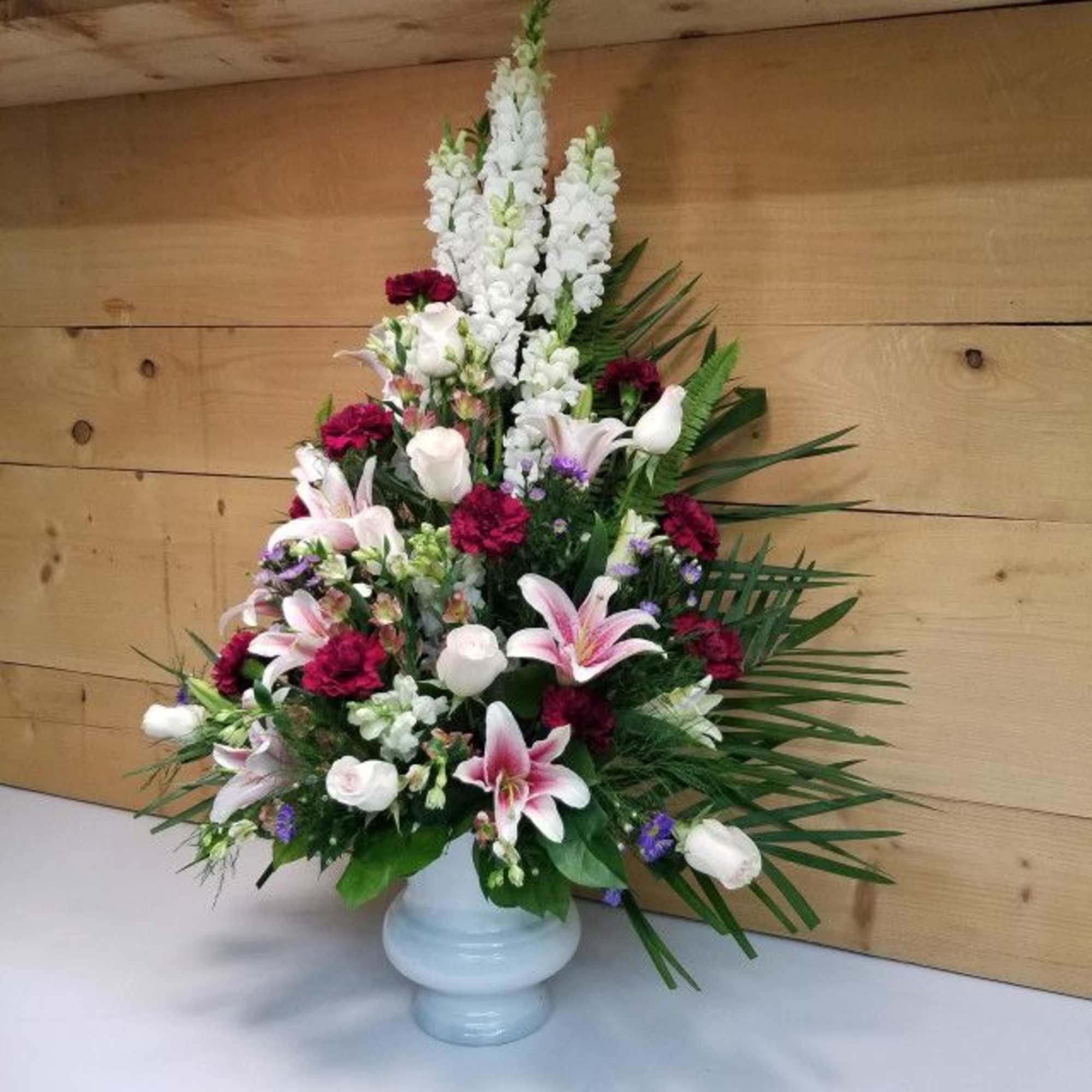 Tall floral arrangement with white lilies, white snapdragons, and burgundy blooms in a white vase.