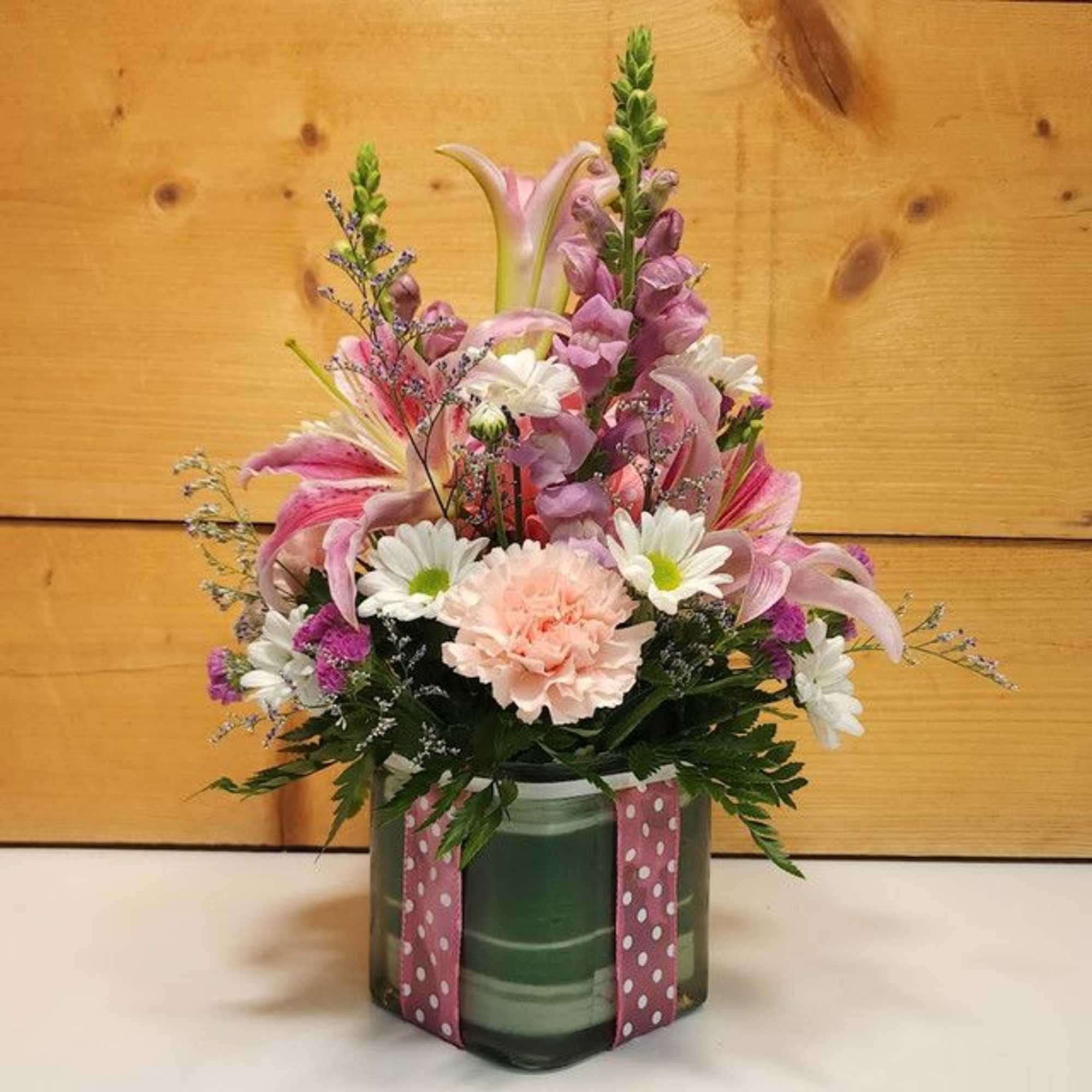 Pink and white mixed flower arrangement in a glass vase with a polka-dot ribbon