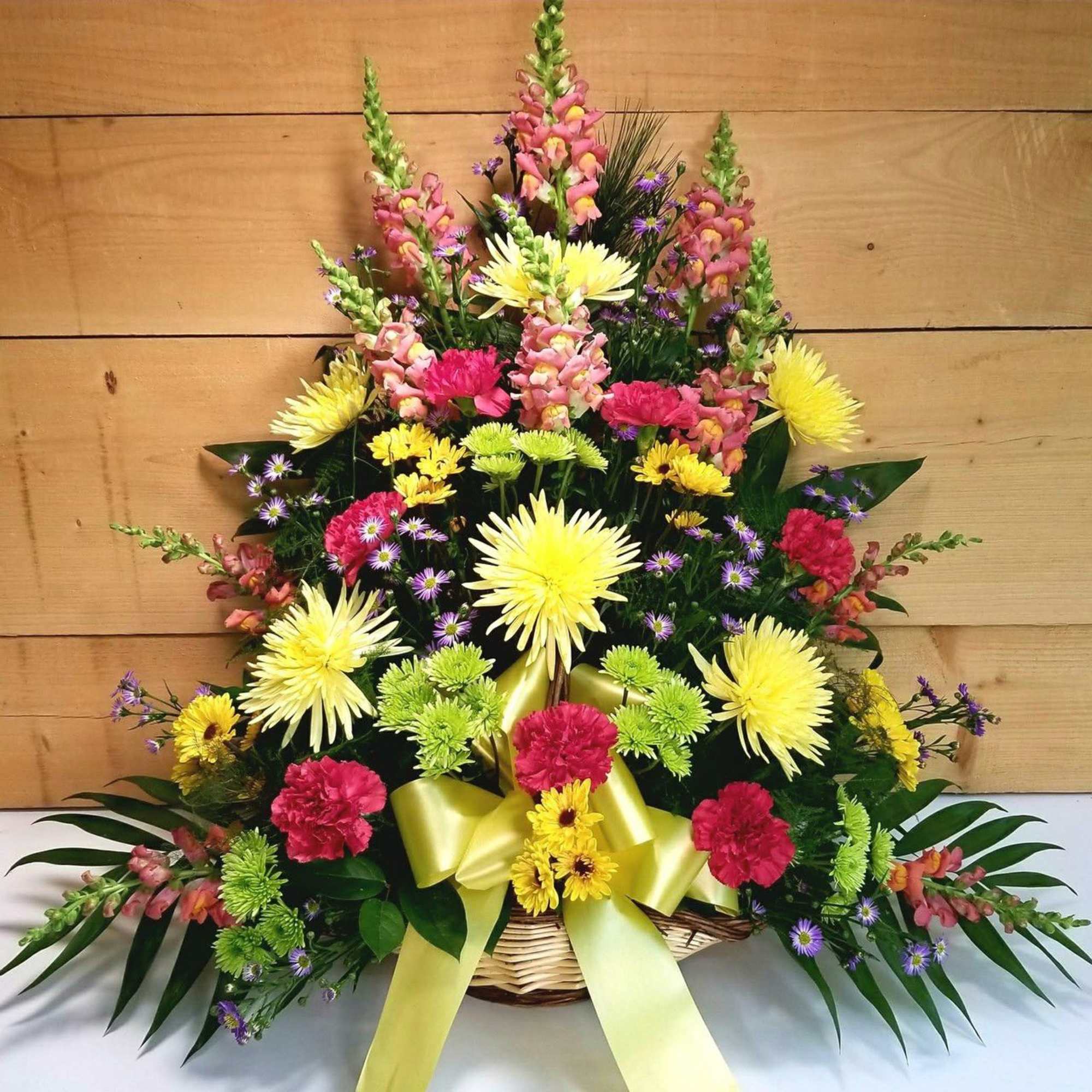 Basket arrangement of yellow, pink, and green flowers with a yellow ribbon