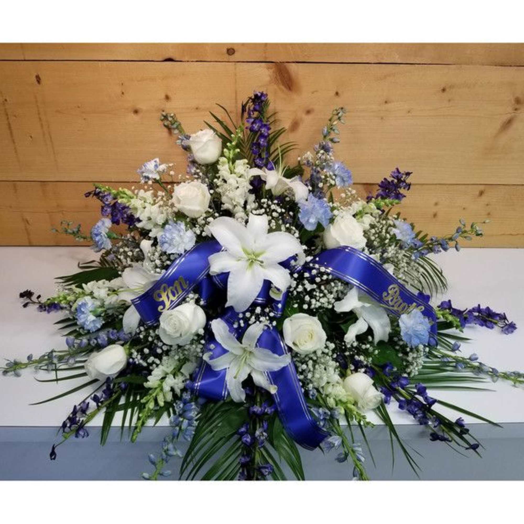 White lilies and roses with blue flowers and ribbons in a large spray