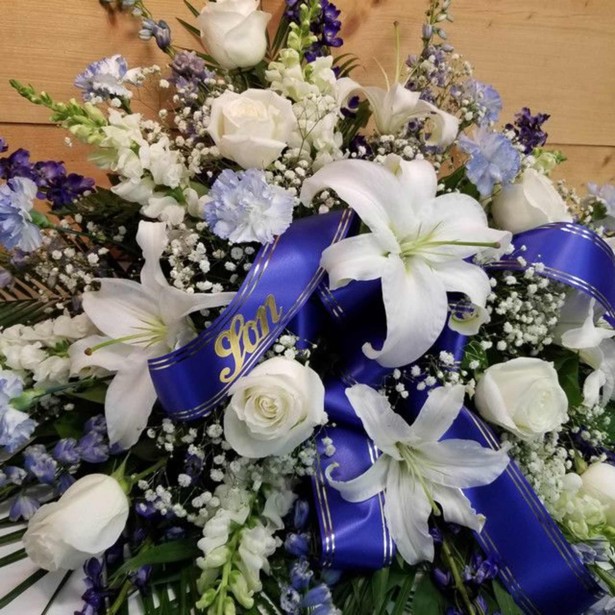 White lilies and roses with blue ribbon accents in a floral spray