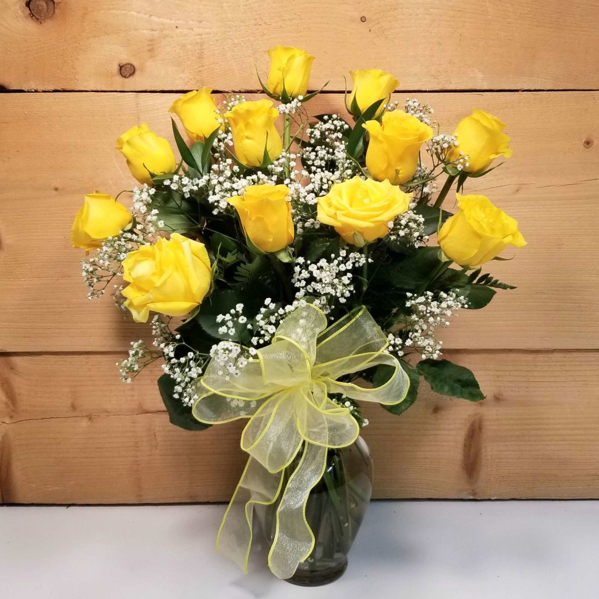 Yellow roses in a glass vase with baby's breath and a yellow ribbon