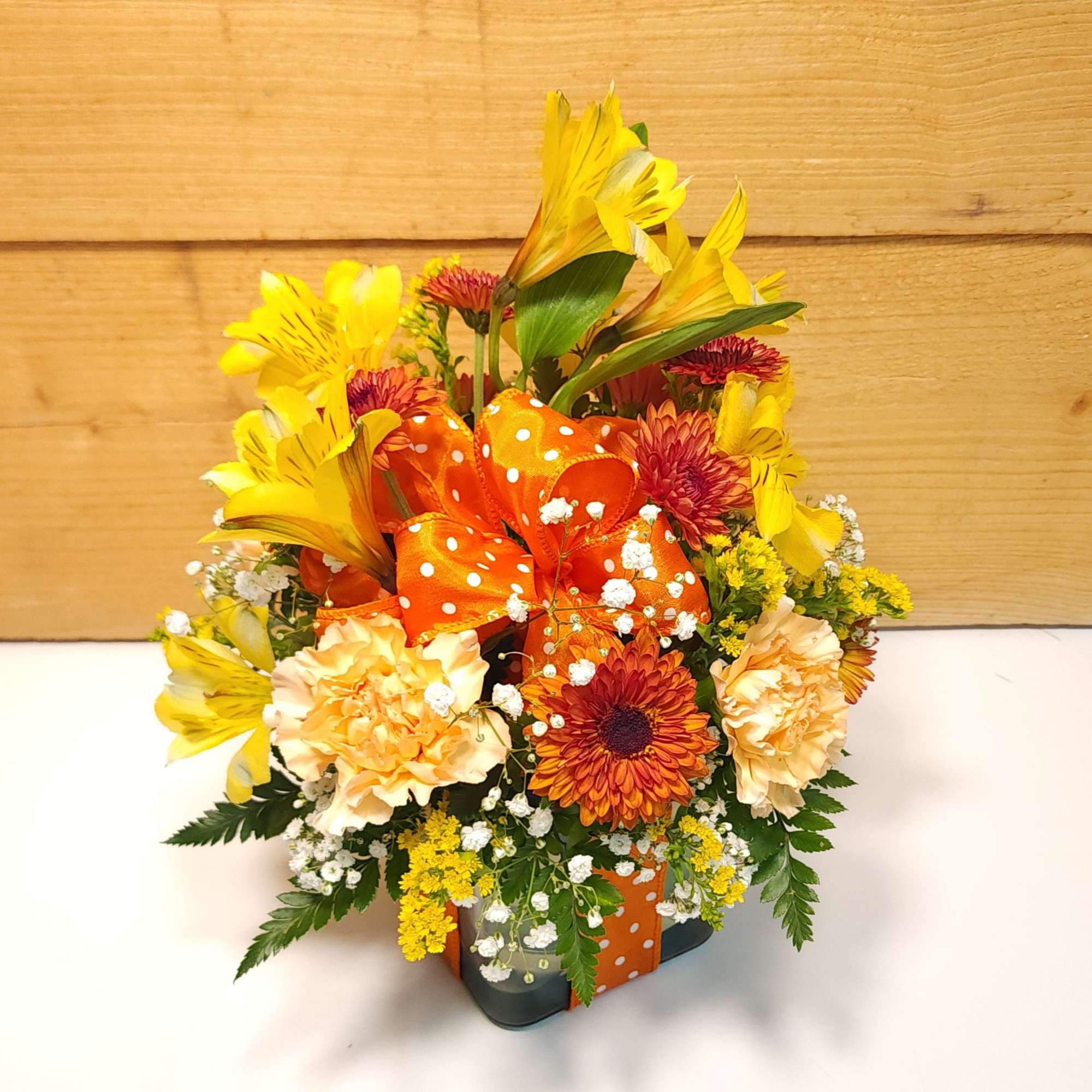 Orange and yellow mixed flower arrangement in a polka-dot container
