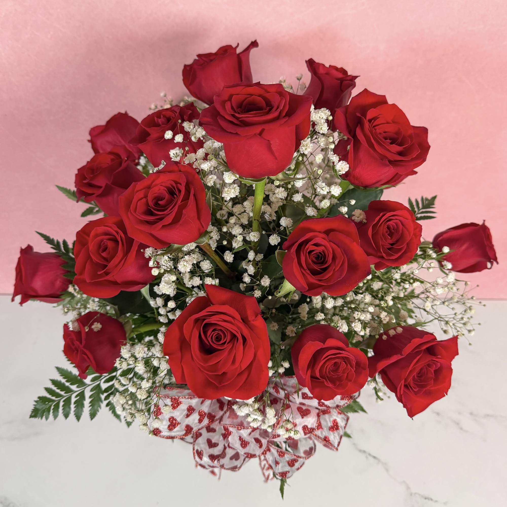 Arrangement of red roses with white filler flowers and heart-print ribbon