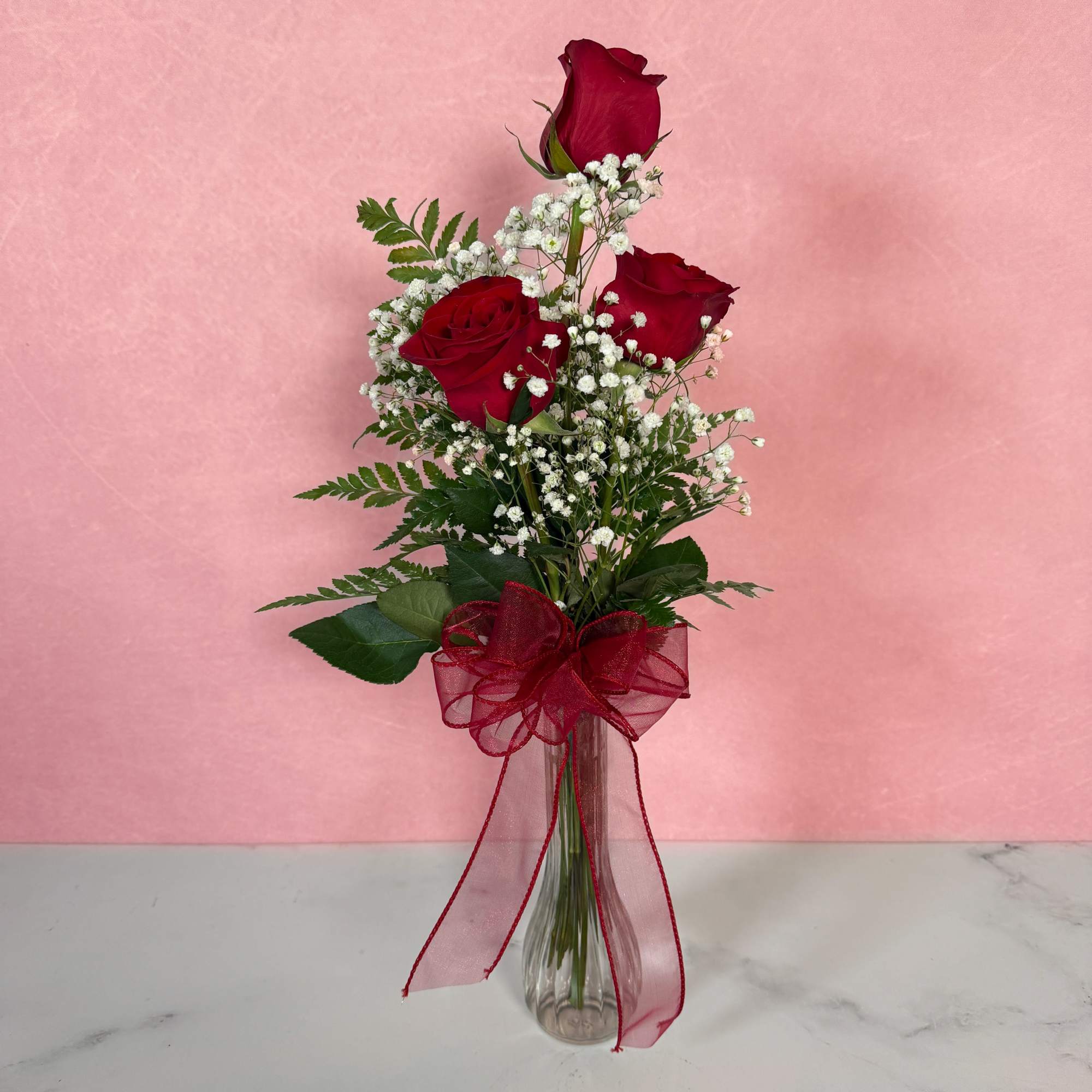 Three red roses in a clear vase with baby's breath and a red ribbon, photo 2 of 3