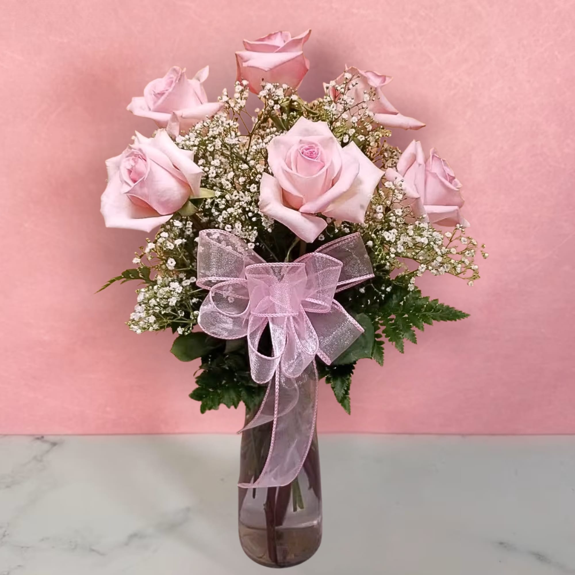 Pink roses arranged in a clear glass vase with a pink ribbon bow