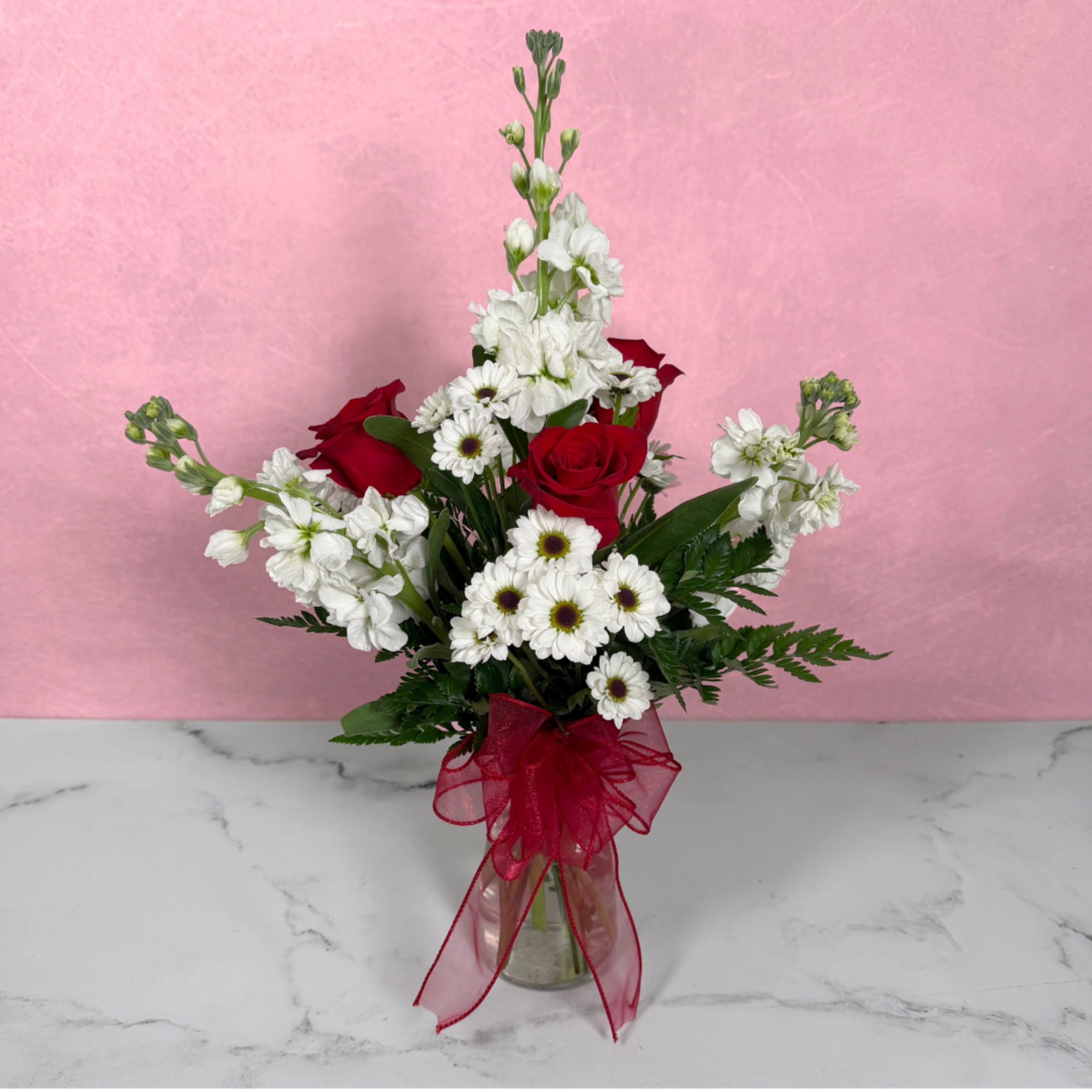 Red roses and white flowers in a glass vase with a red ribbon