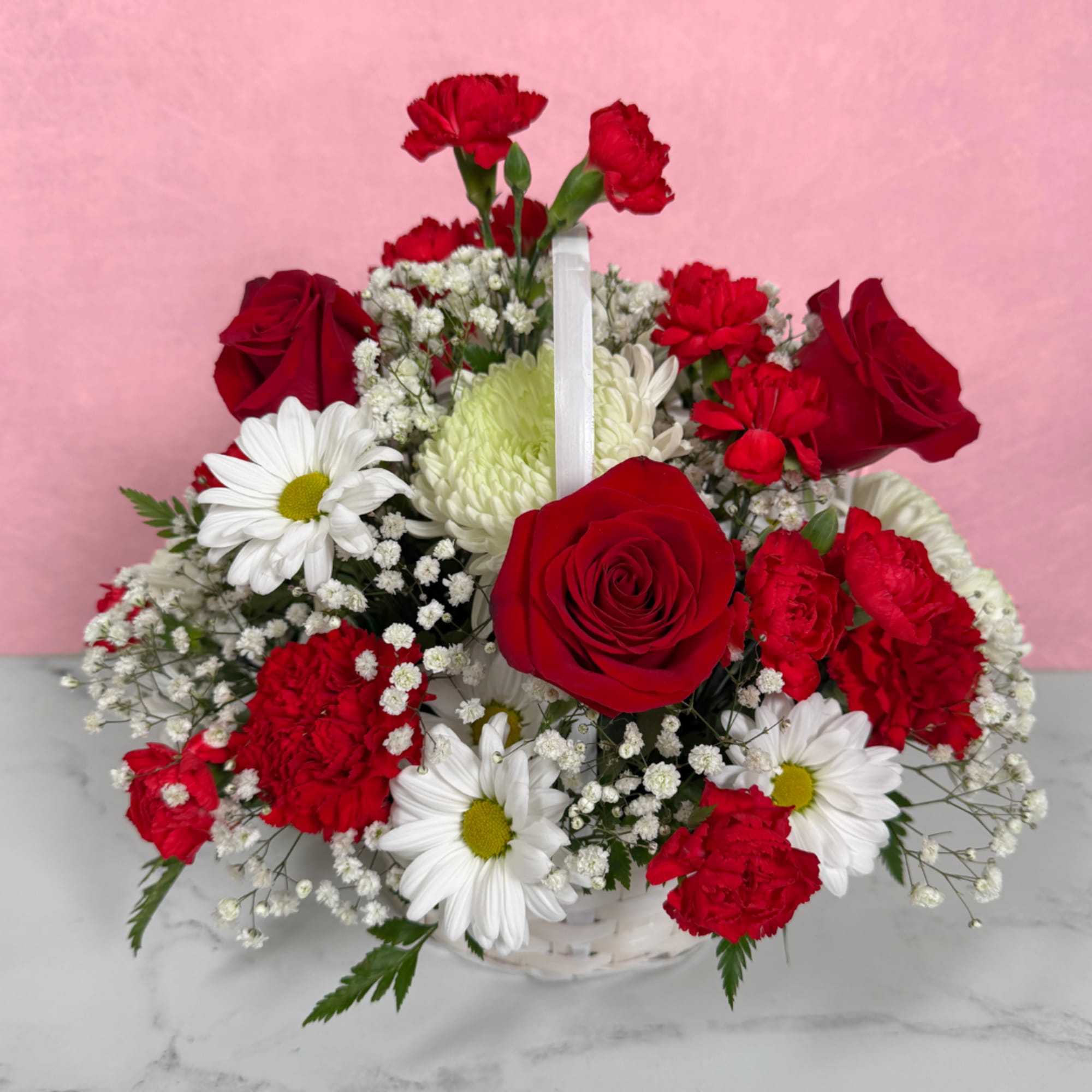 Basket arrangement of red roses, red carnations, and white daisies