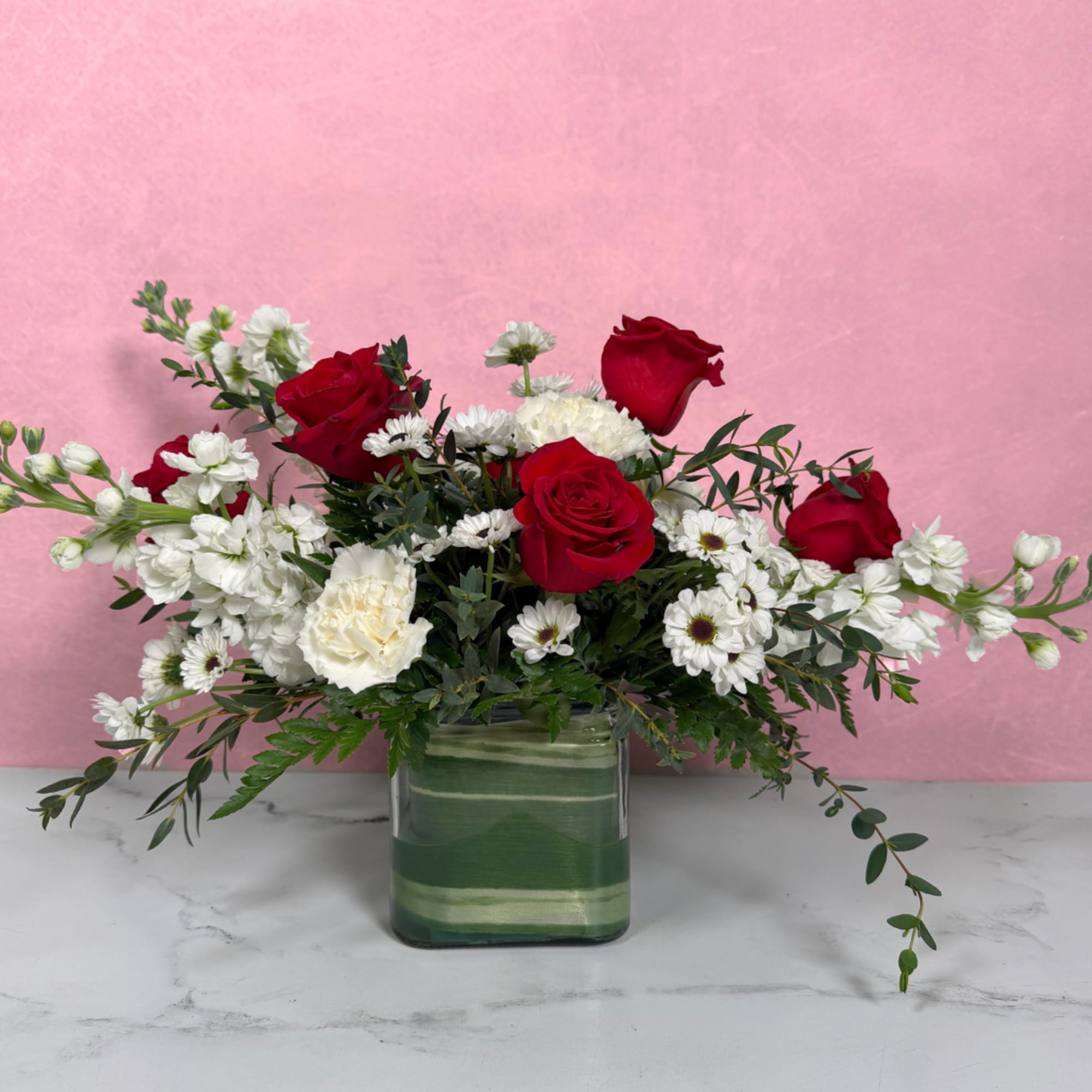 Red roses and white flowers in a green glass vase