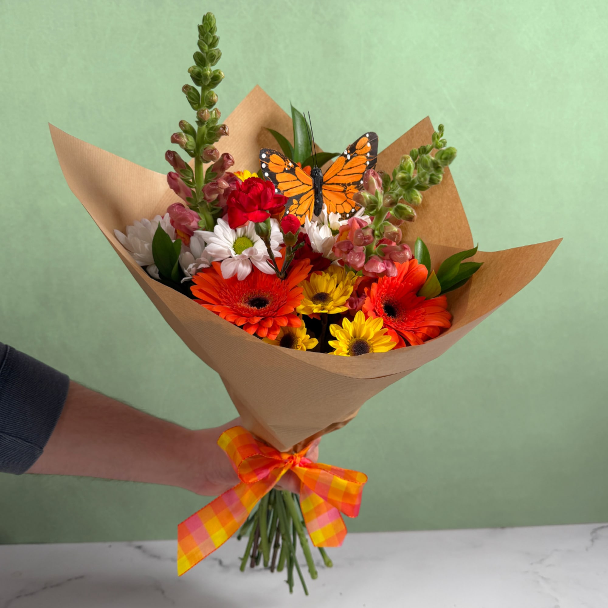 Bright mixed bouquet of orange gerberas and yellow daisies wrapped in kraft paper with a butterfly decoration